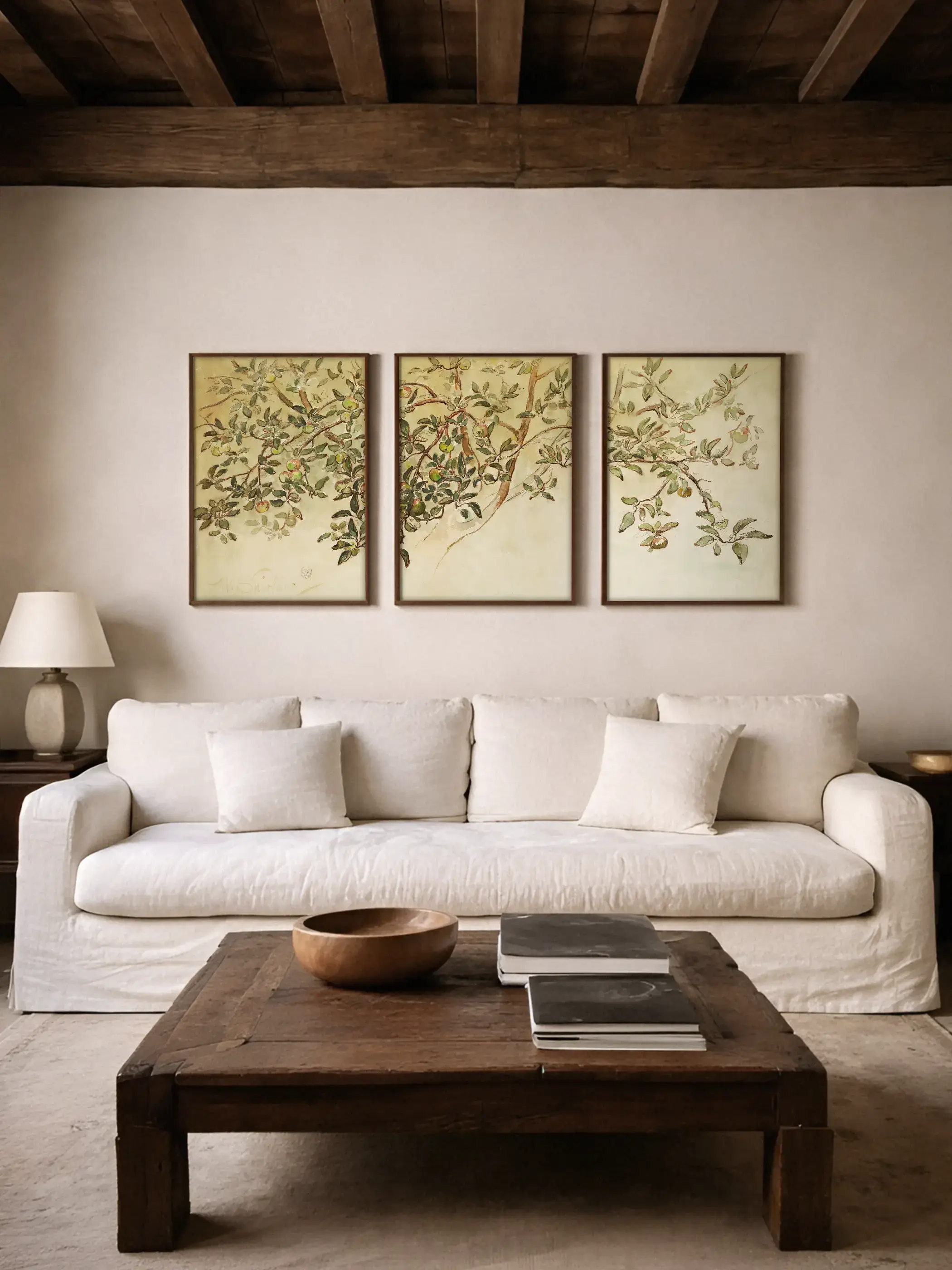 Drei botanische Kunstdrucke mit Apfelzweigen und zarten Blättern hängen über einem hellen Sofa im Wohnzimmer. Die sanften Grün- und Cremetöne schaffen eine ruhige Galerie-Wand im Vintage-Stil.