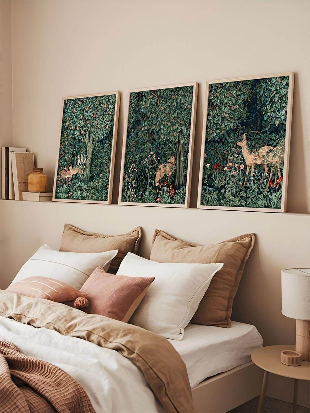 Drei gerahmte Vintage-Kunstdrucke im Stil von William Morris zeigen Reh, Hase und Fuchs in dichtem Blattwerk. Die Szene verleiht dem Schlafzimmer mit warmen Textilien eine nostalgische, naturverbundene Atmosphäre.