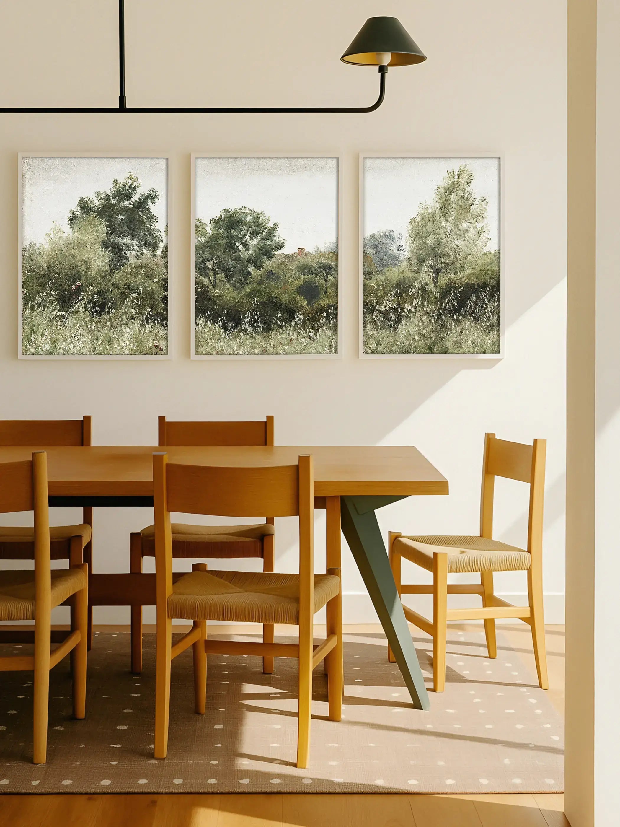 Drei gerahmte Landschafts-Kunstdrucke mit sanften Grüntönen und locker gemalten Bäumen hängen über einem Holztisch im hellen Esszimmer. Das ruhige Triptychon schafft eine natürliche, luftige Atmosphäre und wirkt als harmonische Galerie-Wand.