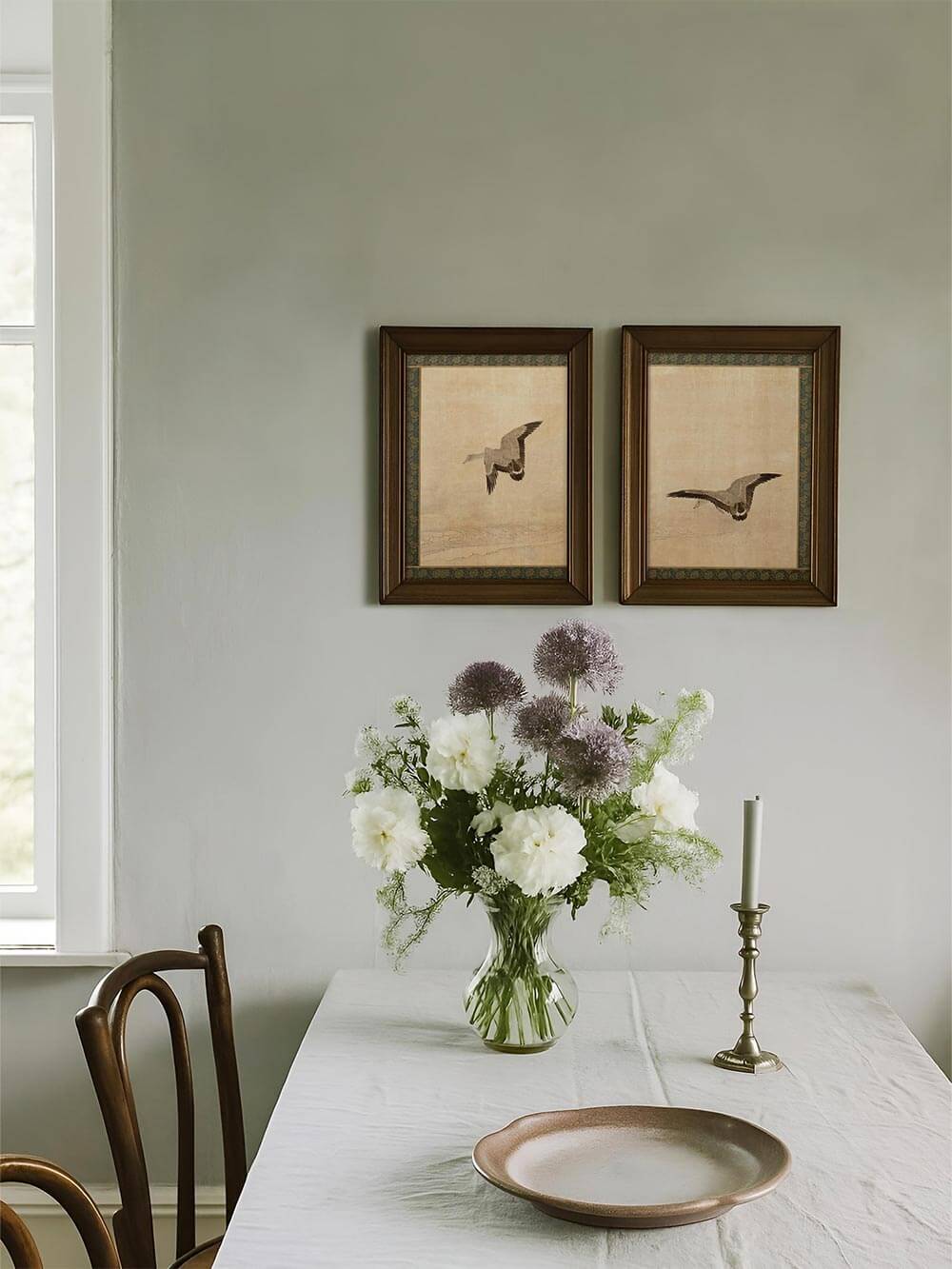 Das Gänse-Diptychon hängt gerahmt über einem gedeckten Esstisch mit Wildblumenstrauß. Die minimalistischen Drucke unterstreichen die nostalgisch-ländliche Einrichtung.