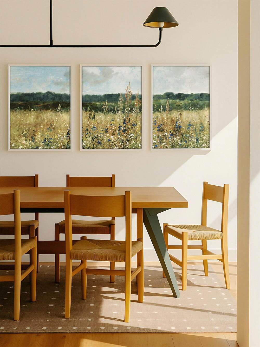 Das Triptychon mit Wiesenmotiv hängt über einem Esstisch aus Holz in heller, moderner Umgebung. Die florale Landschaft verleiht dem Raum eine freundliche, geerdete Atmosphäre.