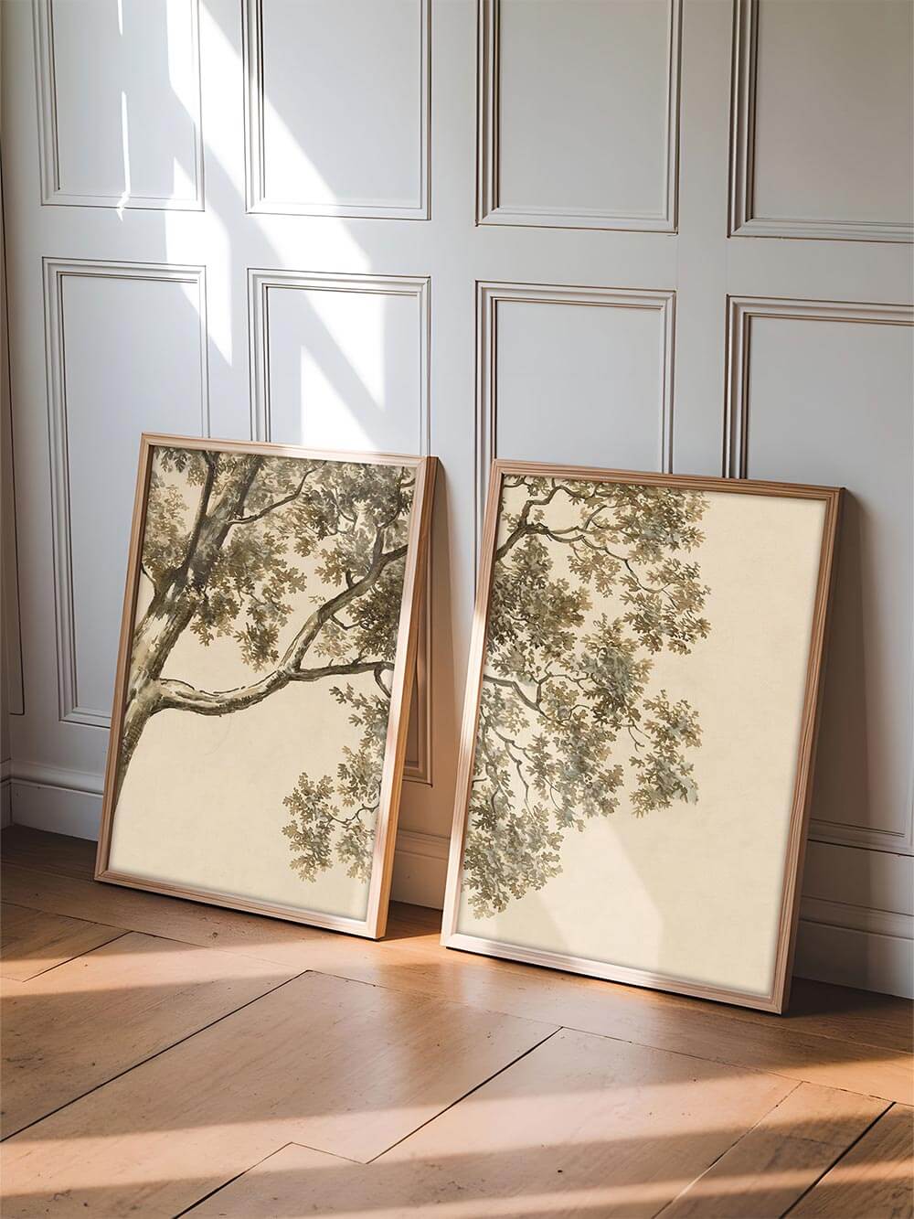 Zwei gerahmte Baum-Kunstdrucke lehnen an einer hellen Wand mit klassischer Vertäfelung und warmem Lichteinfall. Die Szene zeigt das Bilderset als flexible Wanddekoration oder Poster für Wohnzimmer, Flur oder Schlafzimmer.