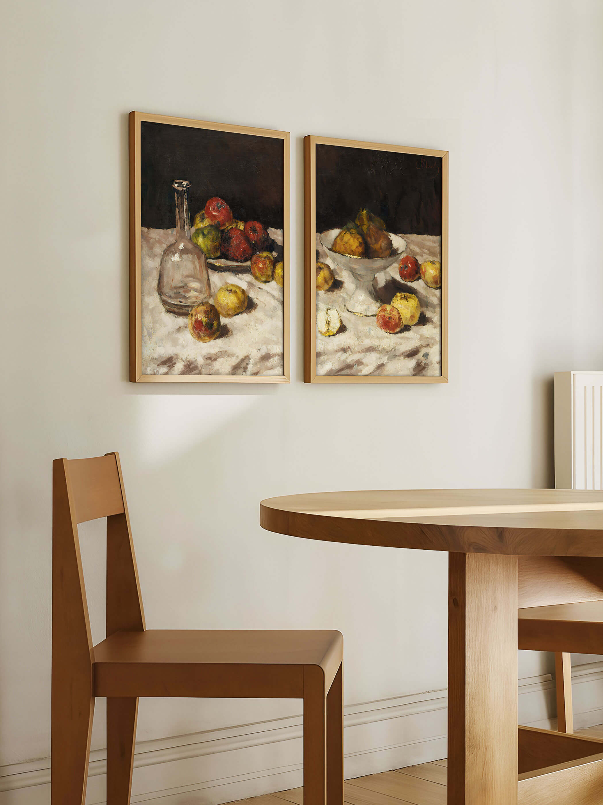 Zwei gerahmte Stillleben Kunstdrucke hängen über einem Esstisch aus Holz in einem hellen Raum. Die Darstellung von Früchten und Keramik ergänzt das natürliche Interieur und wirkt als stilvolle Galerie-Wand im Essbereich.
