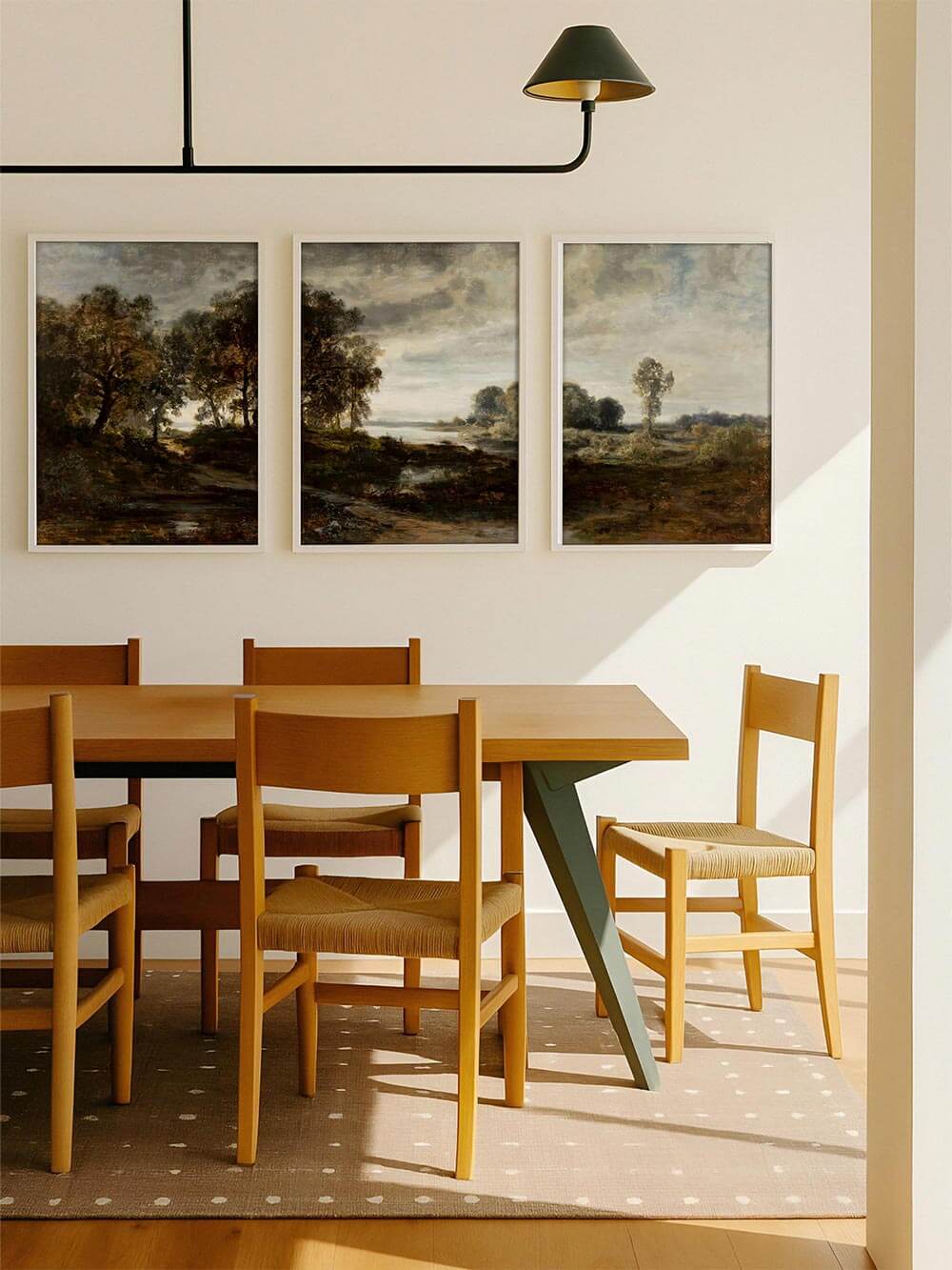Dreiteiliges Landschafts-Wandbild über einem Holztisch im Esszimmer mit hellem Licht und ruhiger Raumgestaltung. Das moody Triptychon schafft einen harmonischen Kontrast zur modernen Einrichtung und verbindet klassische Landschaftsmalerei mit zeitloser Wohnästhetik.
