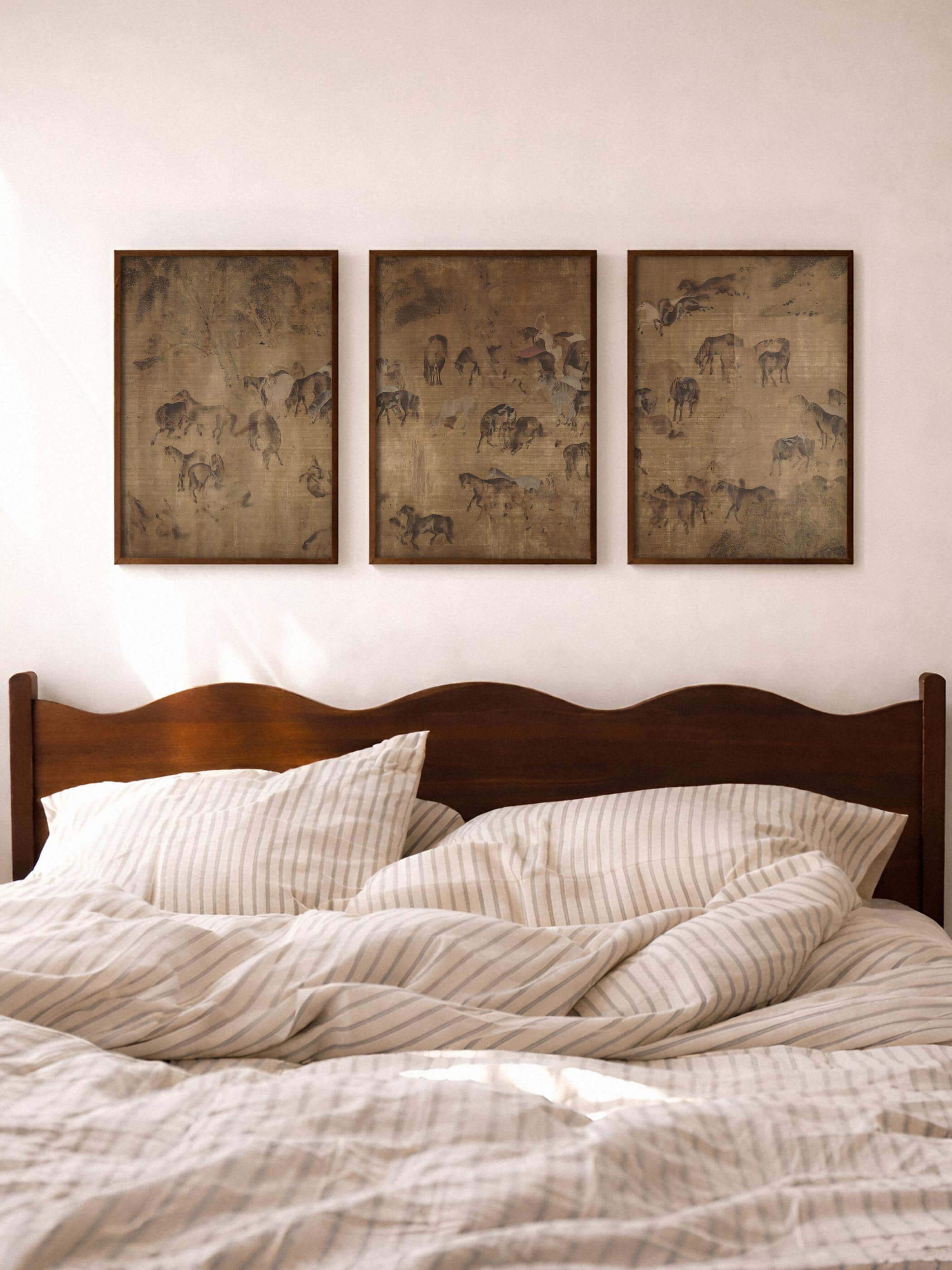 Dreiteiliges Pferde-Wandbild in warmen Naturtönen hängt über einem Bett mit heller, gestreifter Bettwäsche. Die ruhige Komposition schafft eine entspannte Atmosphäre und wirkt als harmonisches Kunstdruck Set im Schlafzimmer.