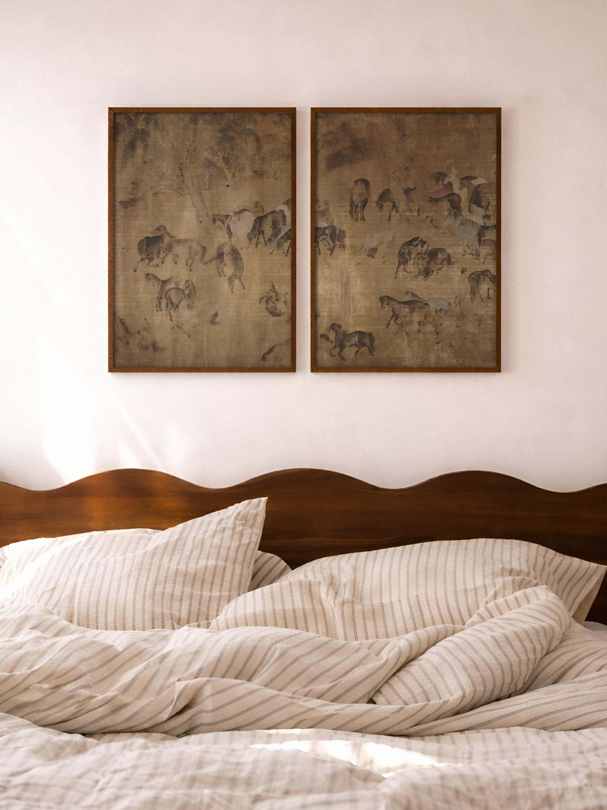 Zwei gerahmte Pferde-Kunstdrucke hängen über einem Bett mit heller, gestreifter Bettwäsche. Die warmen Erdtöne und die ruhige Komposition schaffen eine entspannte Atmosphäre und wirken als harmonische Wanddekoration im Schlafzimmer.