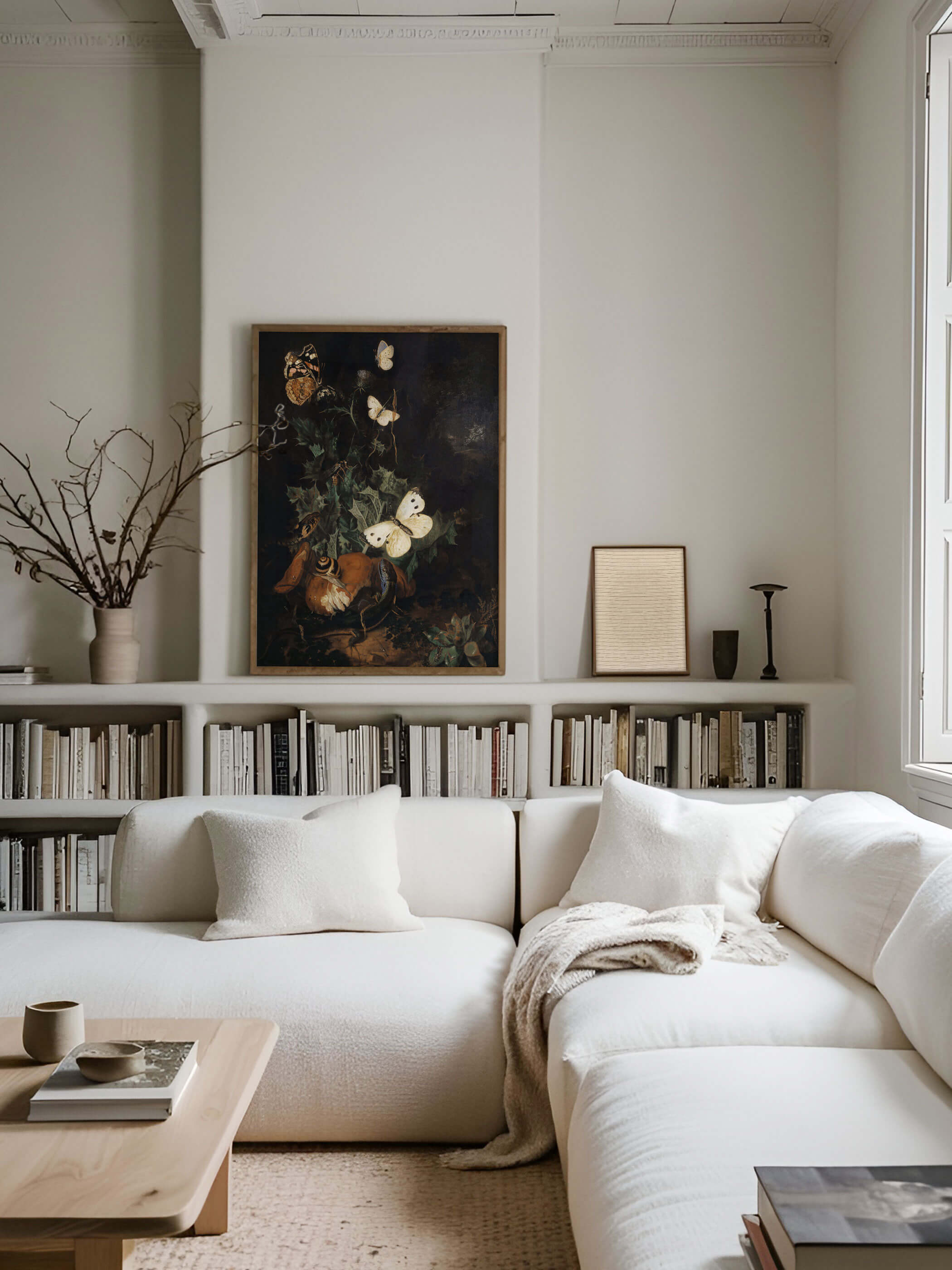 Dunkles Barock-Stillleben mit Schmetterlingen und Pflanzen, in einem modernen Wohnzimmer über einem Bücherregal und einer weißen Couch aufgehängt. Eine stimmungsvolle Wanddekoration für klassische und zeitgenössische Räume.