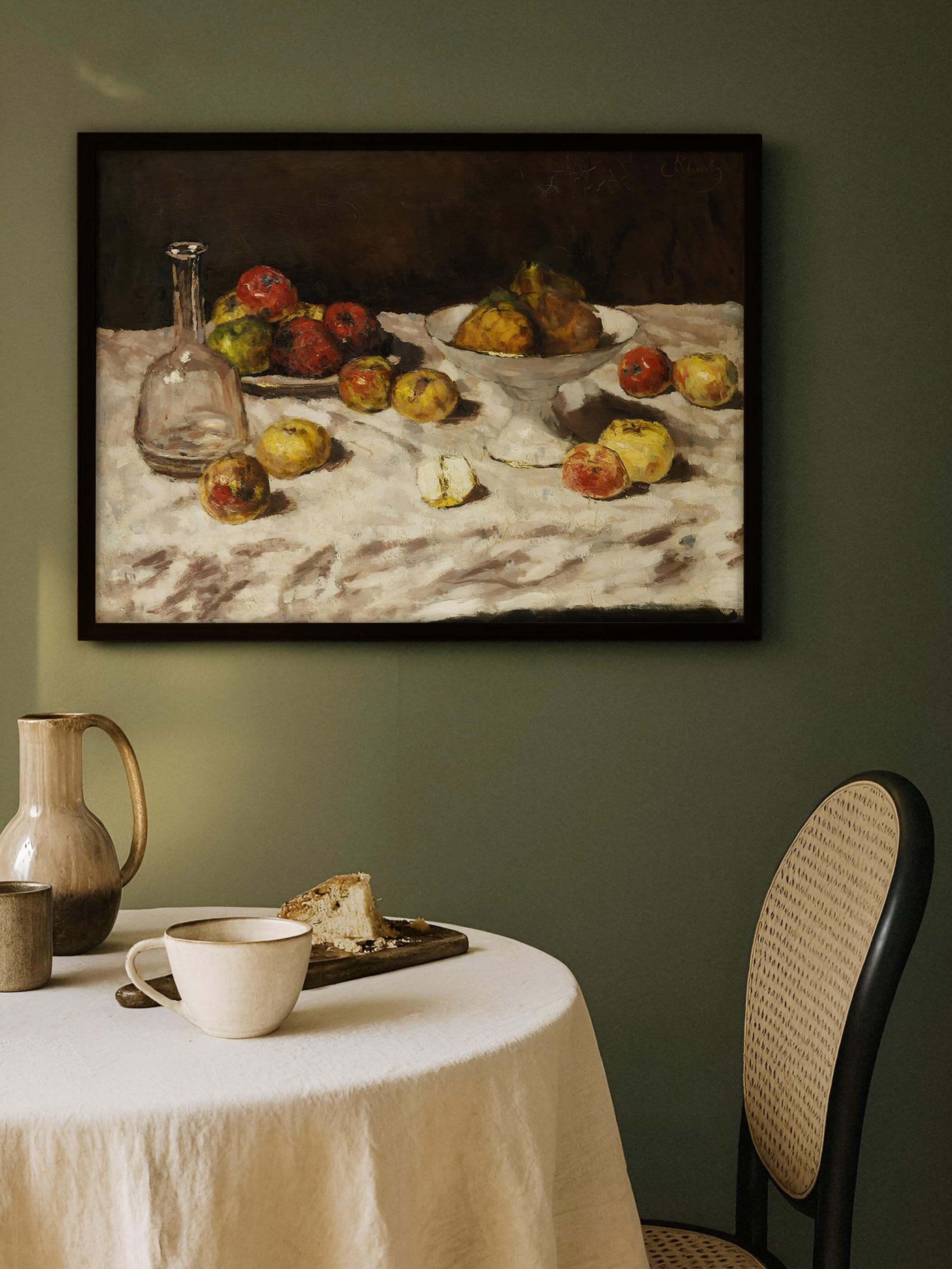 Dunkel gerahmter Kunstdruck mit Apfel- und Birnenstillleben hängt an einer salbeigrünen Wand über einem gedeckten Tisch mit Tasse und Kuchen. Das warme Wandbild setzt einen erdigen Akzent im gemütlichen Esszimmer.