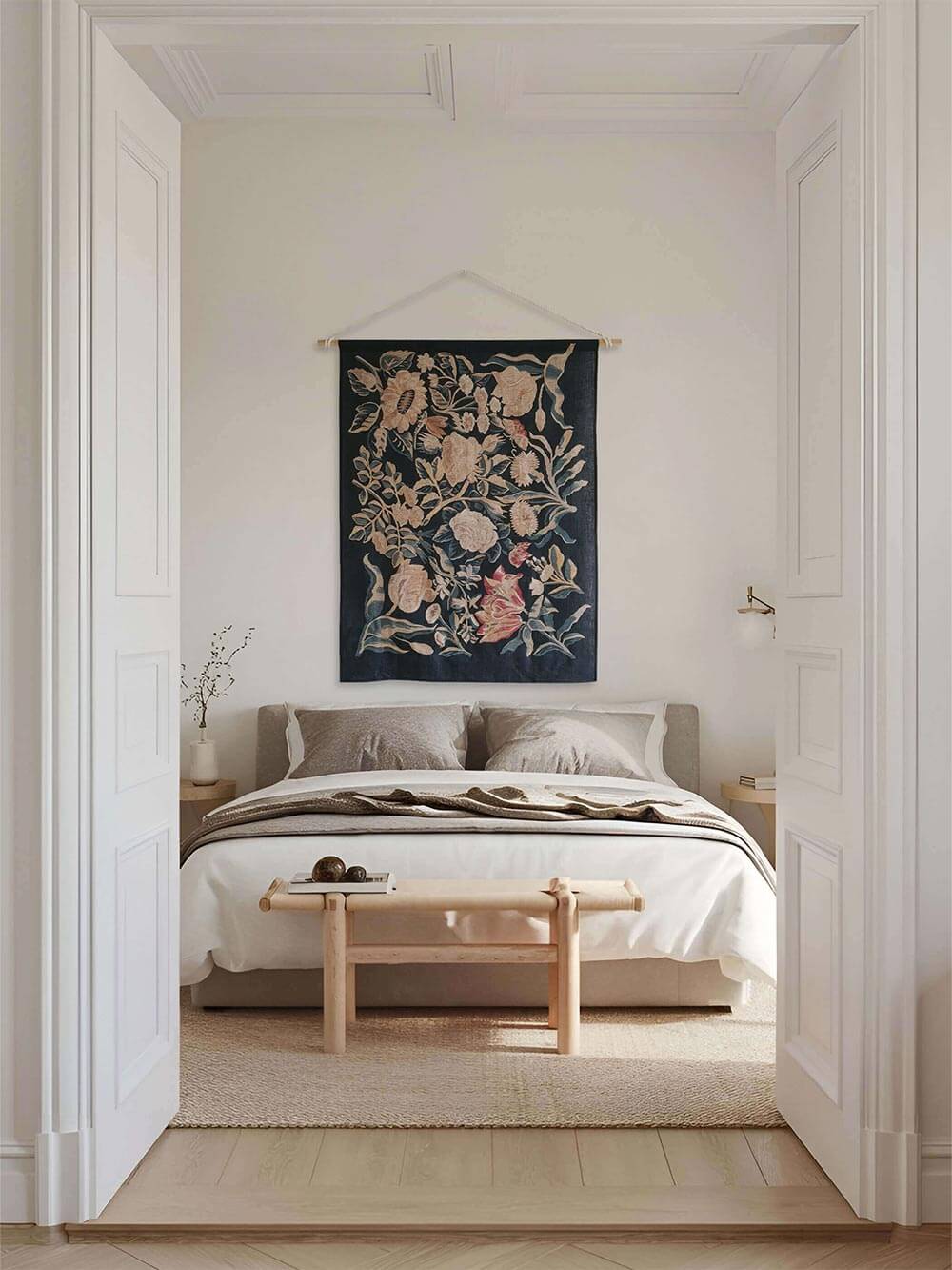 Leinen-Wandbehang mit Blumenmotiv hängt zentriert über einem Bett in einem hellen, ruhigen Schlafzimmer. Die weichen Farben und das textile Material schaffen eine warme, entspannte Atmosphäre mit natürlicher Eleganz.