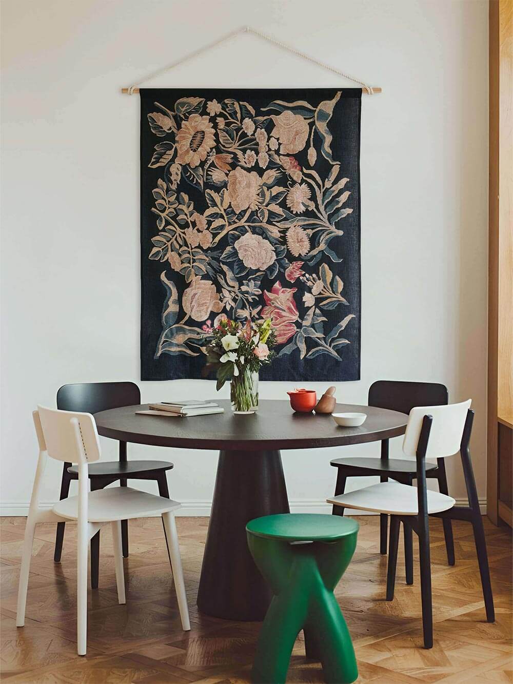Leinen-Wandbehang mit floraler Stickoptik in Beige, Blau und Altrosa hängt über einem runden Esstisch in einem modernen Esszimmer. Das textile Wandbild verbindet Vintage-Blumenmotiv mit zeitgemäßer Einrichtung und wirkt ruhig und kunstvoll.