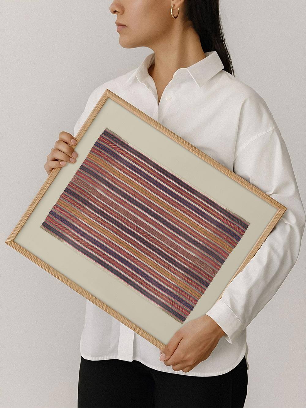 Gerahmter Kunstdruck mit gestreiftem Textilmotiv wird von einer Person gehalten und zeigt die Proportionen im Vergleich zum Körper. Das Bild vermittelt anschaulich die Größe des Posters und eignet sich zur besseren Einschätzung für die Wandgestaltung.