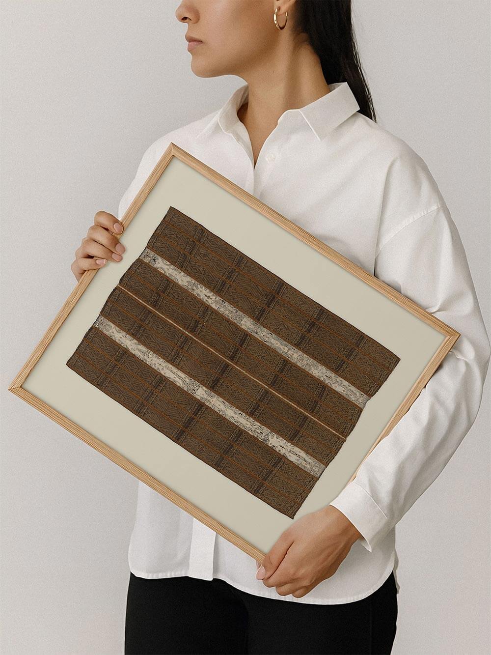 Eine Person hält den gerahmten Kunstdruck mit dunklem, strukturiertem Textilmotiv vor neutralem Hintergrund. Die Aufnahme zeigt die Proportionen des Posters und unterstreicht die handwerkliche Anmutung des Designs für moderne Wohnräume.