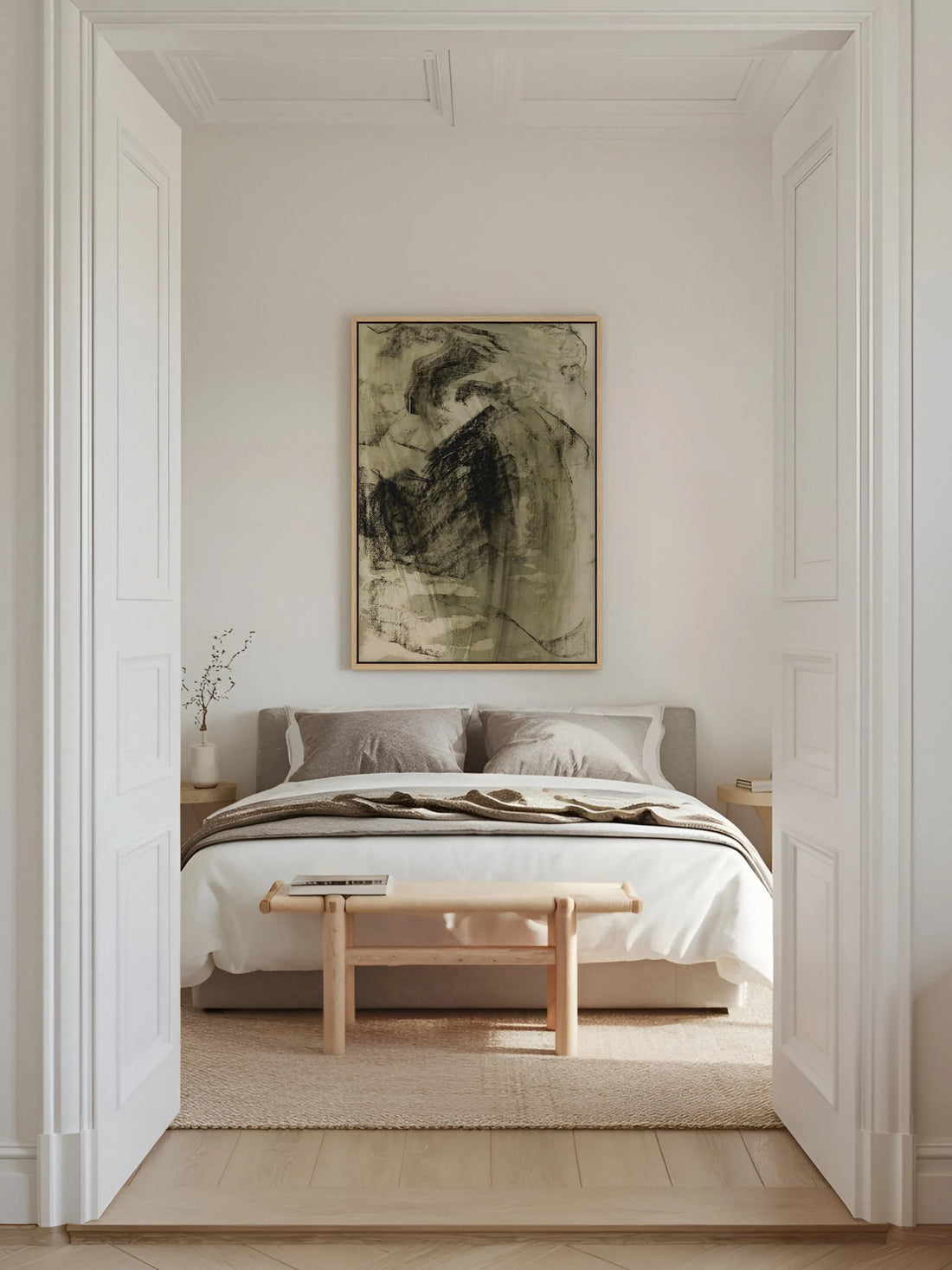 Abstraktes Leinwandbild in Schwarz und Oliv im Naturholzrahmen über einem Bett mit grauem Polsterkopfteil in einem hellen Altbauschlafzimmer. Das dunkle Wabi Sabi Wandbild bildet den Ruhepunkt des Raums.