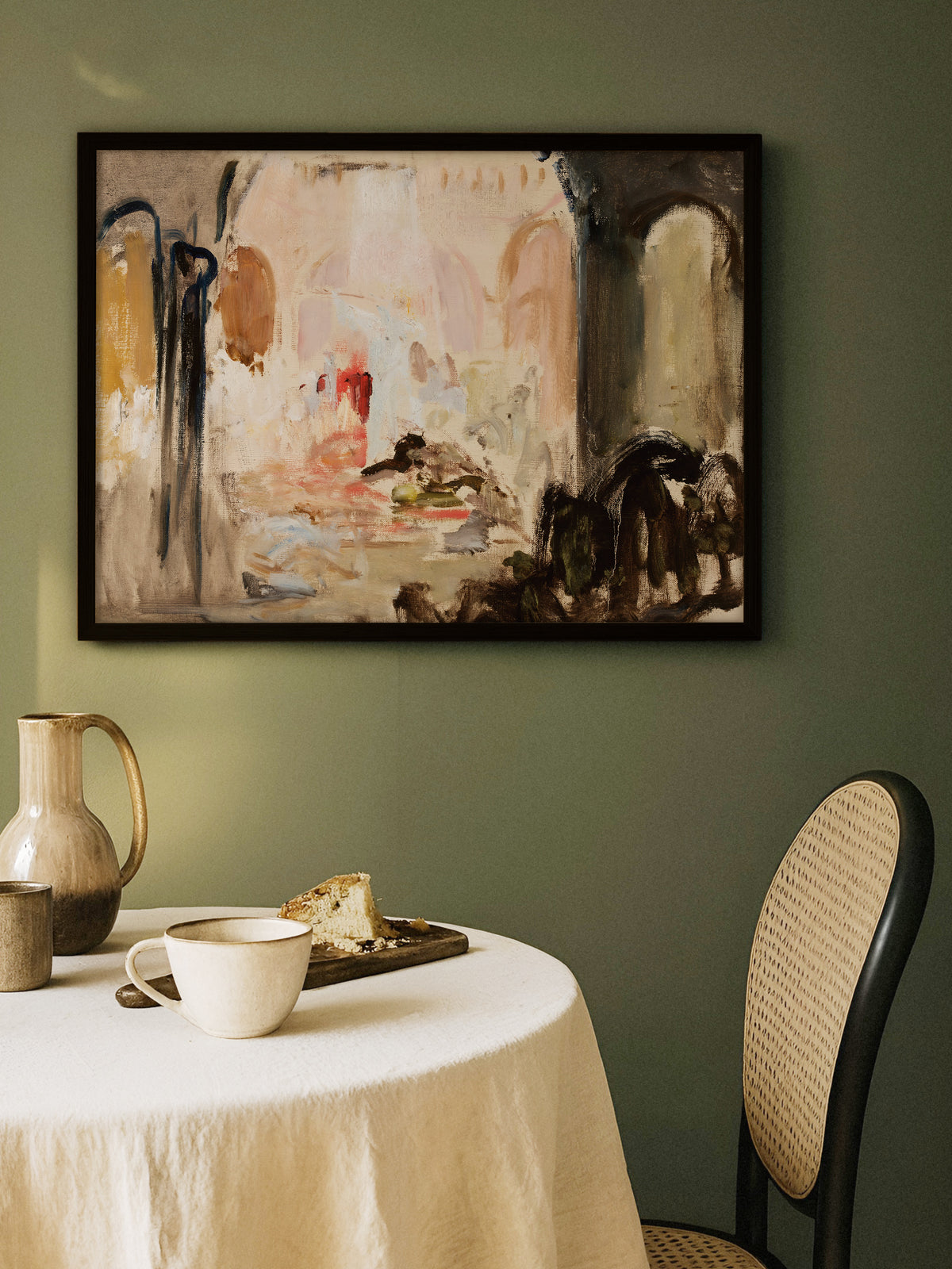 Abstrakter Kunstdruck in Beige, Rosé und Braun im schwarzen Rahmen an einer olivgrünen Wand über einem runden Tisch mit Leinentischdecke, Keramikkrug und Tasse. Das Wabi-Sabi-Wandbild bringt ruhige Wärme ins Esszimmer.