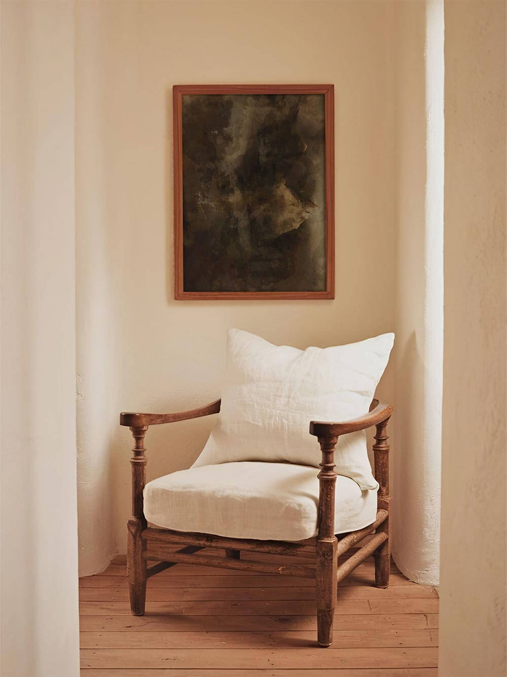 Abstraktes Wandbild über einem rustikalen Holzstuhl in einer hellen Wandnische schafft einen stillen, kontemplativen Moment. Die gedeckten Farben des Posters harmonieren mit warmem Holz und natürlichem Licht.