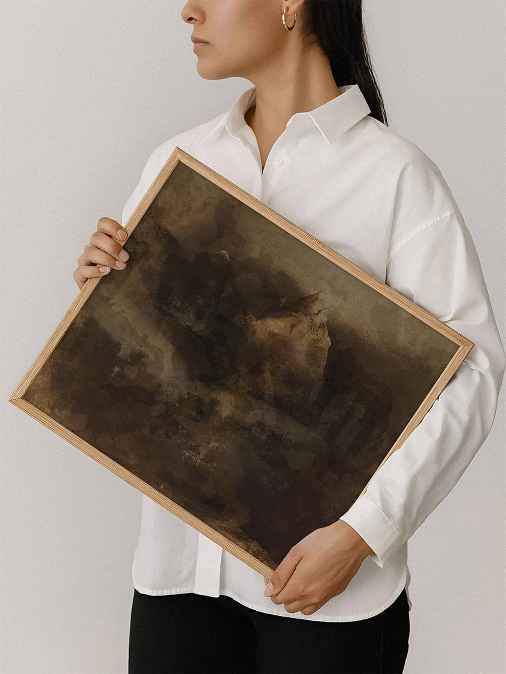 Eine Person hält den gerahmten abstrakten Kunstdruck vor neutralem Hintergrund und zeigt Format und Wirkung des Wandbilds. Die dunkle Farbpalette und die weiche Struktur unterstreichen den modernen, wabi-sabi Stil.