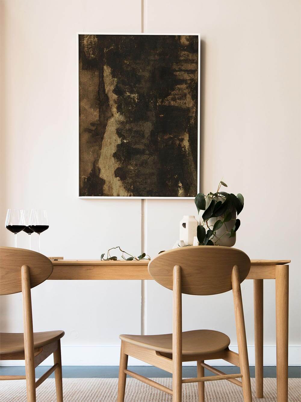 Abstrakter Wabi-Sabi Kunstdruck in dunklen Braun- und Schwarztönen hängt über einem Esstisch aus hellem Holz. Die reduzierte Einrichtung und natürlichen Materialien unterstreichen die ruhige, zeitlose Wirkung des Wandbilds im Essbereich.