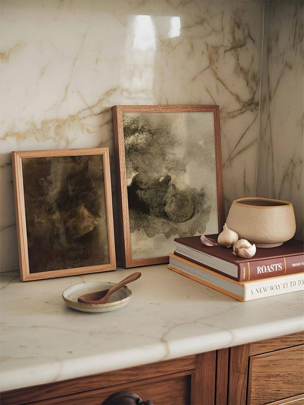 Zwei abstrakte Kunstdrucke im Holzrahmen stehen auf einer hellen Marmorfläche neben Büchern und Keramik. Die warmen Beige- und Grautöne schaffen eine ruhige, natürliche Atmosphäre und passen ideal zu moderner Küchen- oder Wohnraumdeko.