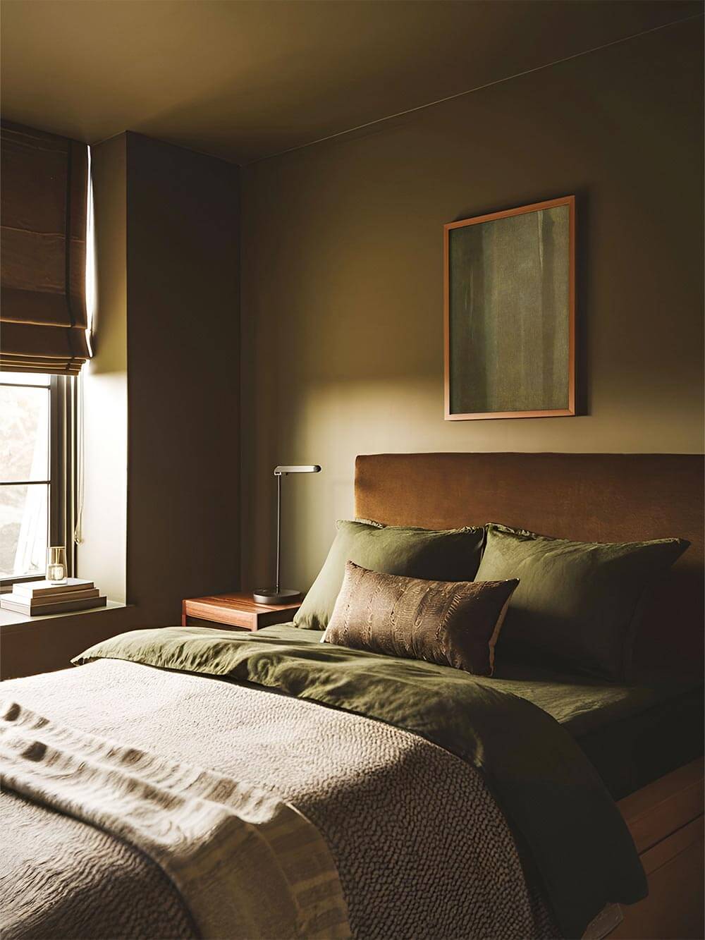 Grüner abstrakter Kunstdruck über dem Bett in einem warm beleuchteten Schlafzimmer, bei dem die sanften Naturtöne mit Textilien und Wandfarbe harmonieren und eine entspannte, moody Atmosphäre für moderne Wohnräume schaffen.