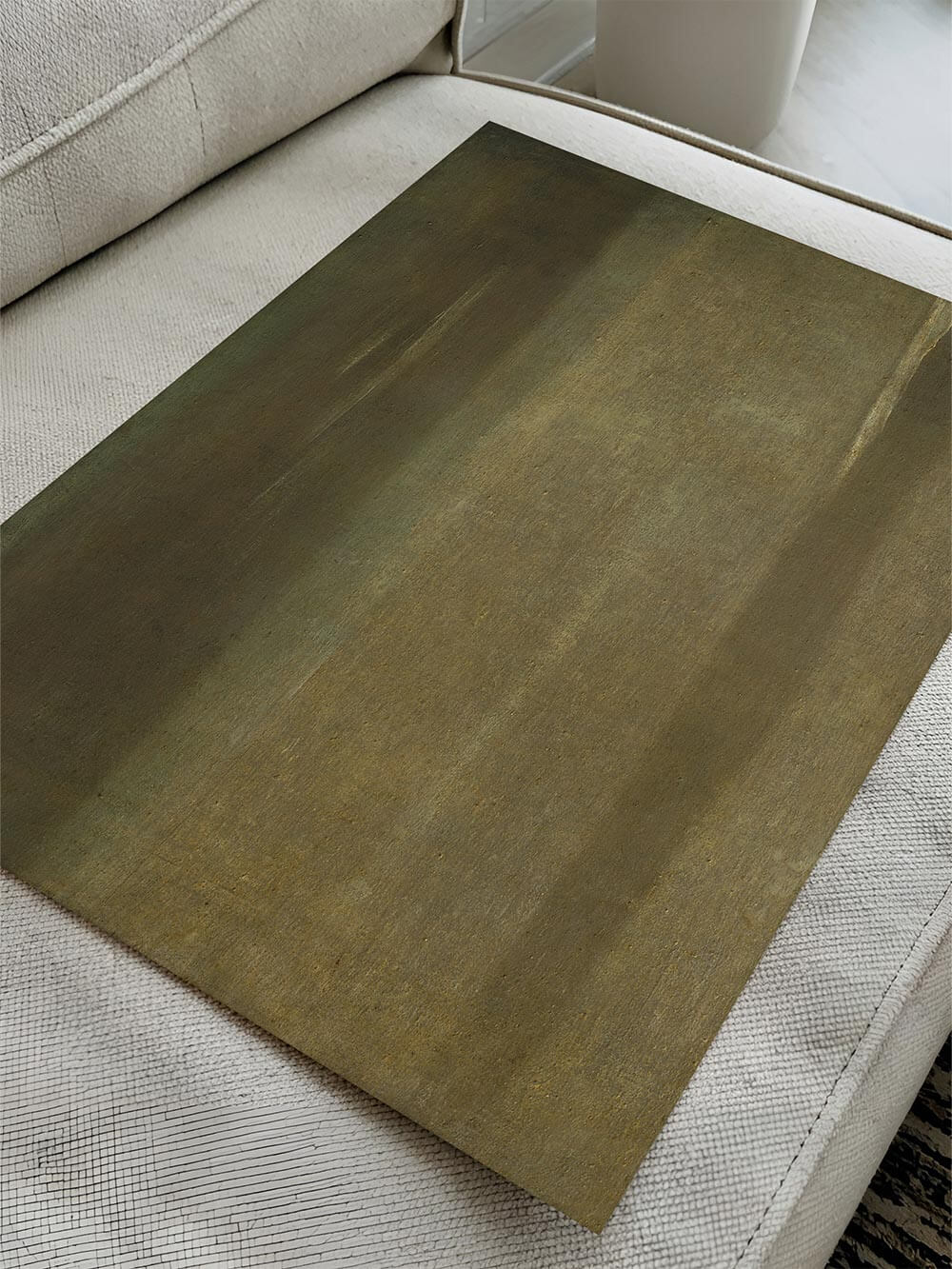 Grüner abstrakter Kunstdruck liegt flach auf einem hellen Sofa und zeigt sanfte vertikale Farbnuancen in Moos- und Olivtönen, wodurch Materialität, matte Anmutung und zeitlose Wirkung des Wandbilds sichtbar werden.