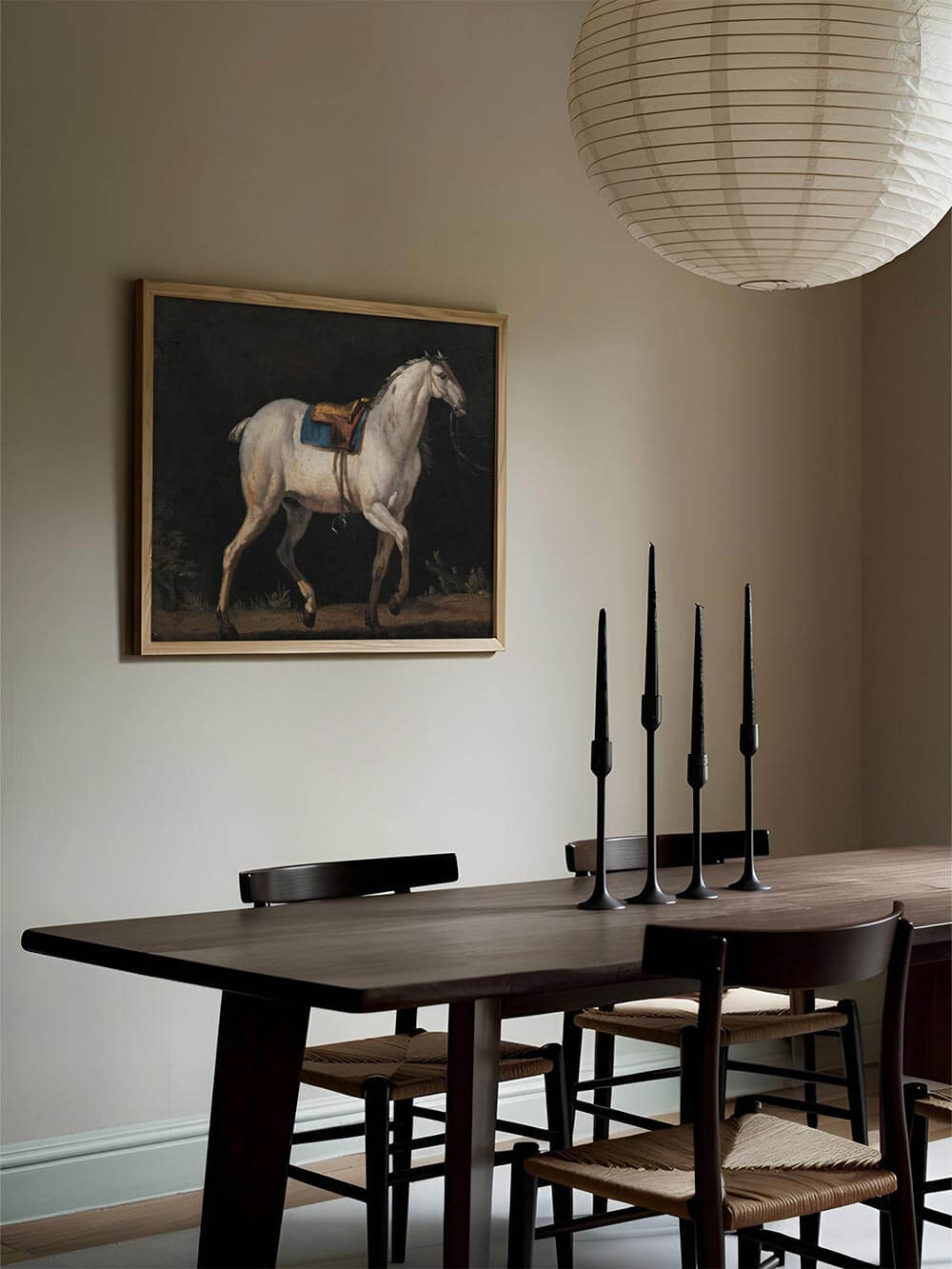 Vintage Kunstdruck eines weißen Pferdes mit Sattel vor dunklem Hintergrund, ruhig an der Wand über einem Holztisch inszeniert. Die gedämpfte Farbpalette und klassische Komposition verleihen dem Raum eine elegante, zeitlose Atmosphäre mit kunstvollem Wandbild.