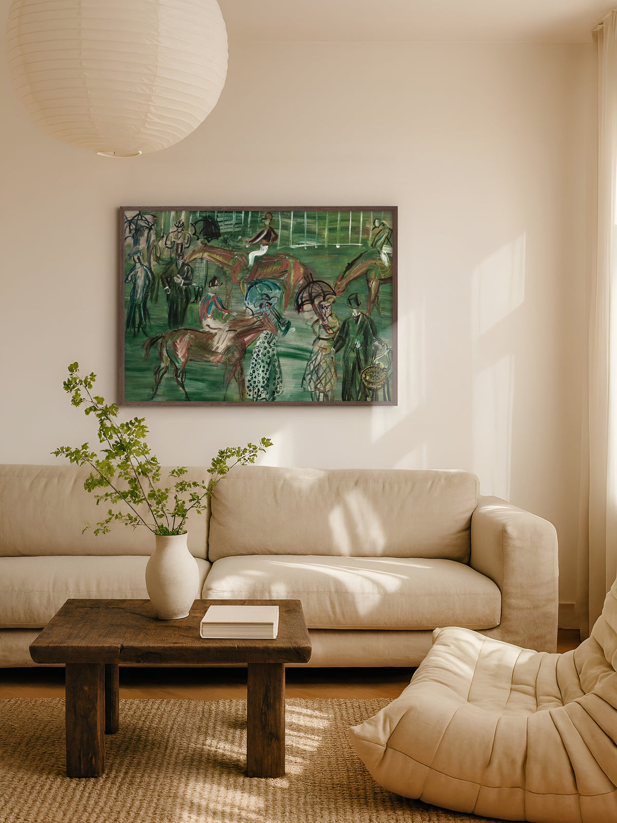 Grünes Pferde Poster im dunklen Holzrahmen über einem beigen Sofa im hellen Wohnzimmer, davor ein rustikaler Couchtisch mit weißer Vase und Zweigen unter einer Papierlampe. Das Vintage Wandbild passt zu einem warmen Japandi Wohnstil.