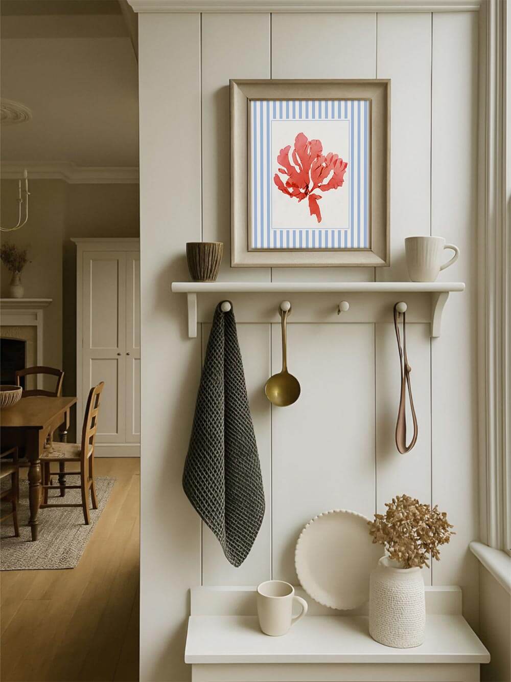 Der maritime Kunstdruck mit roter Alge hängt gerahmt über einer hellen Küchenbank. Das gestreifte Passepartout bringt Leichtigkeit in den Raum im Landhausstil.