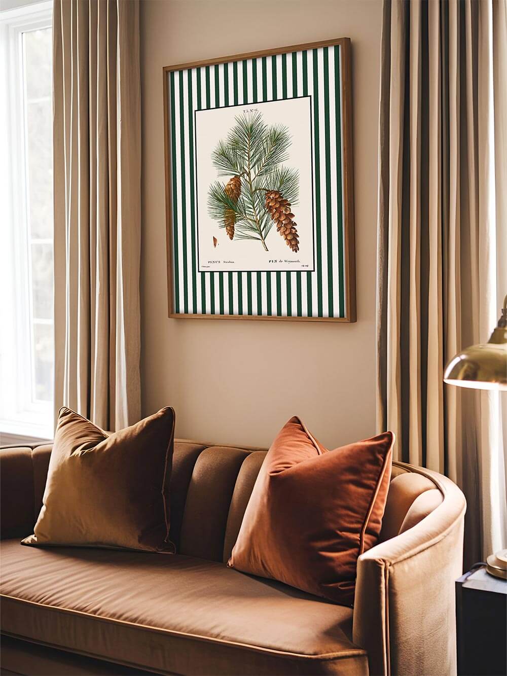 Botanischer Kunstdruck mit grün-weiß gestreiftem Rand über einem samtbraunen Sofa mit kupferfarbenen Kissen, harmonisches Wandbild im klassischen botanischen Stil.