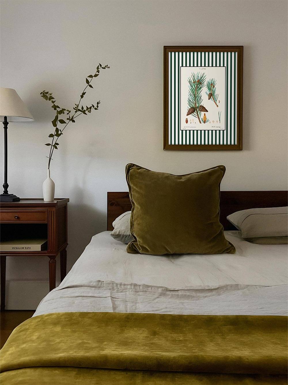 Botanischer Kunstdruck Pin sauvage über Bett mit olivgrüner Samtdecke, warme, natürliche Farbpalette, stilvolles Vintage-Wandbild für das Schlafzimmer.
