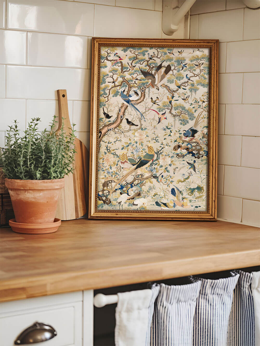 Antiker Chinoiserie-Kunstdruck in einem goldenen Rahmen auf einer Arbeitsplatte in einer stilvollen Landhausküche, umgeben von Küchenutensilien.