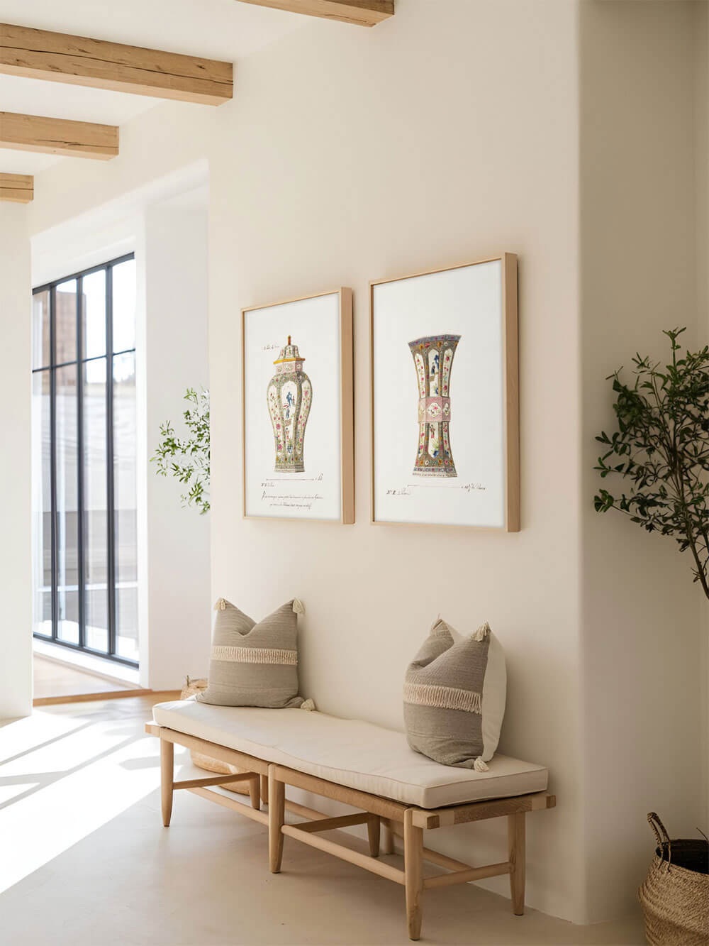 Ein minimalistischer Flur mit zwei gerahmten Kunstdrucken an der Wand, die antike, florale Vasen zeigen. Unter den Bildern steht eine schlichte Holzbank mit beigen Kissen. Die sonnige Atmosphäre und das natürliche Licht lassen die Details der Kunstwerke besonders hervorstechen.