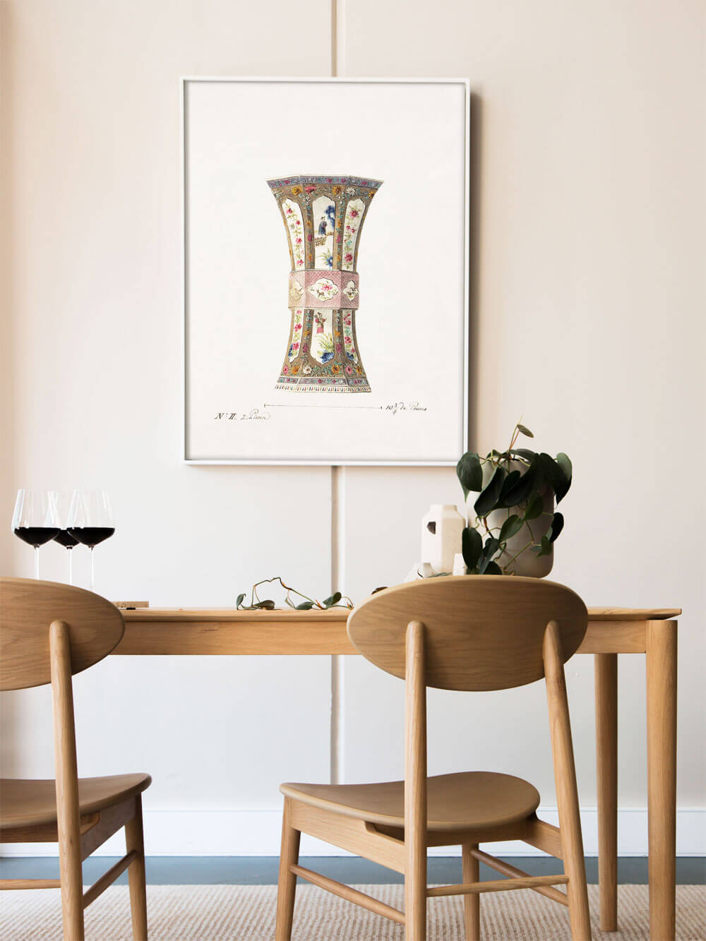 Ein elegant eingerichtetes Esszimmer mit zwei Holzstühlen vor einem Esstisch. An der Wand hängt ein Kunstdruck einer antiken Vase, kunstvoll verziert mit floralen Mustern und farbigen Details in zarten Tönen. Die helle Umgebung und der schlichte Rahmen betonen die Feinheit der Darstellung.