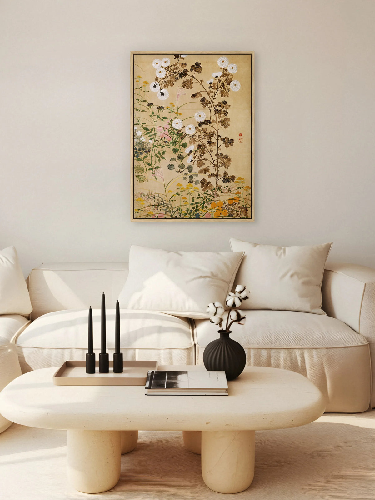 Leinwandbild mit Chrysanthemen im Naturholzrahmen über einem cremefarbenen Sofa, davor ein runder Couchtisch mit schwarzen Kerzen und Baumwollzweigen. Das Chinoiserie Wandbild fügt sich in die hellen Naturtöne ein.