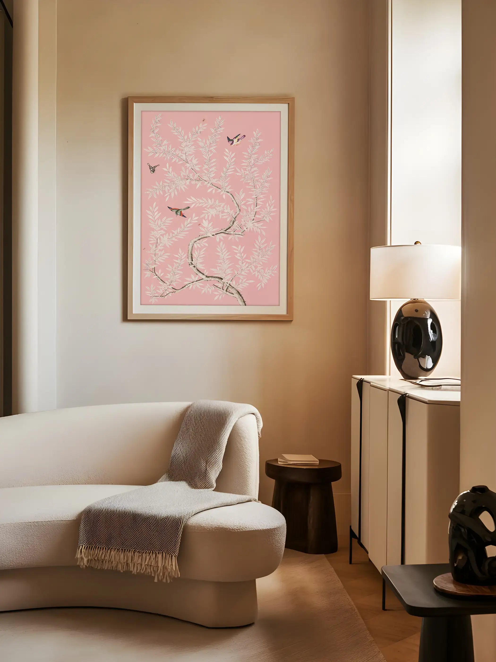 Ein rosa Chinoiserie-Kunstdruck mit weißen Blütenzweigen und fliegenden Vögeln hängt über einem geschwungenen Sofa im Wohnzimmer. Die sanften Farben verleihen dem Raum eine elegante und ruhige Atmosphäre.