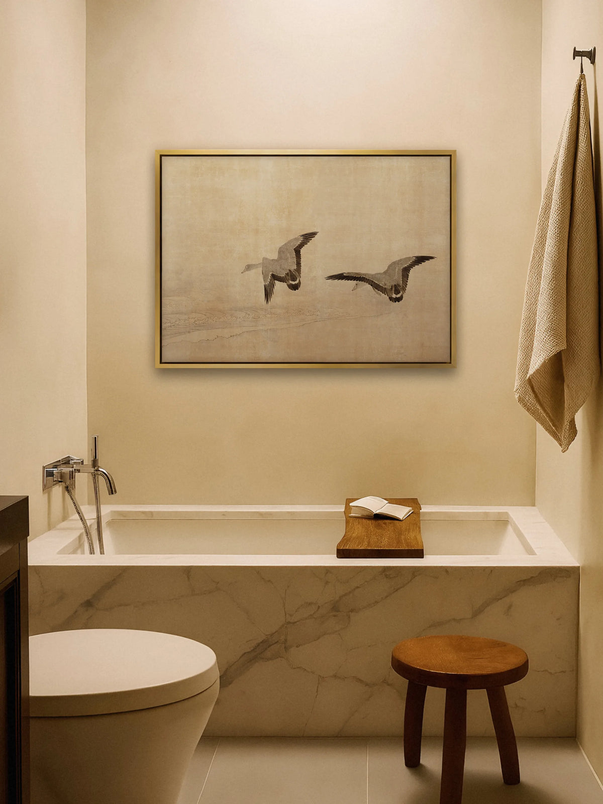 Beiges Leinwandbild mit Gänsen im goldenen Rahmen über einer Badewanne mit Marmorverkleidung. Ein Holzbrett mit aufgeschlagenem Buch liegt über der Wanne, daneben stehen ein Holzhocker und ein Leinenhandtuch am Haken.