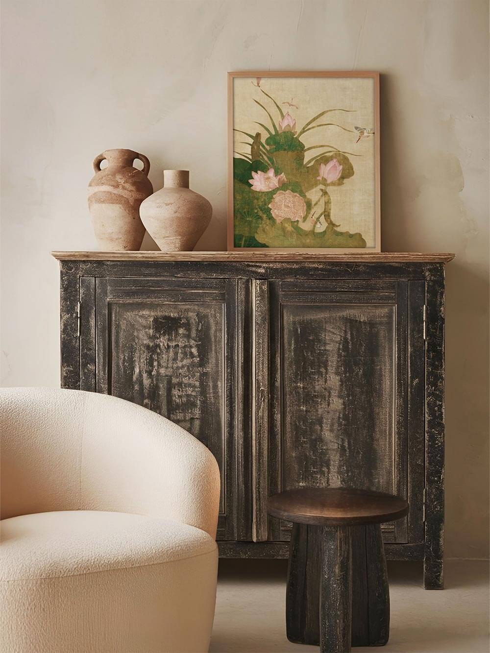 Chinoiserie Kunstdruck mit rosa Blüten auf hellem Grund in schlichter Holzrahmung auf einer dunklen Holzkommode. Das Vintage Wandbild fügt sich stimmungsvoll in die rustikale Wohnzimmereinrichtung ein.