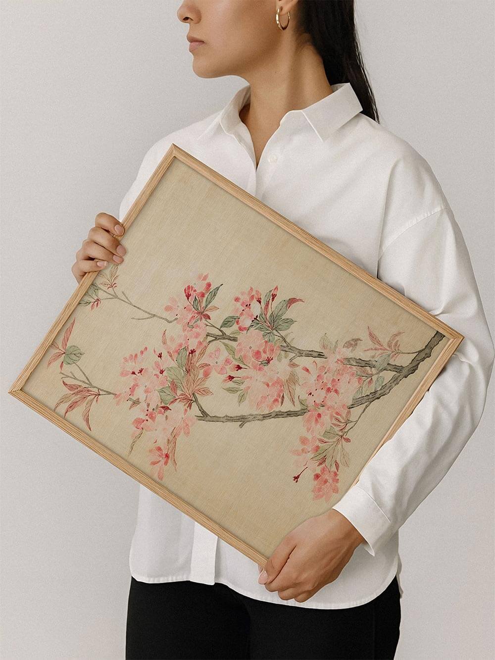 Eine Frau hält den gerahmten Kunstdruck mit zarten rosa Kirschblüten. Die Illustration zeigt feine Linien und eine dezente Farbpalette, die nostalgisch wirkt.