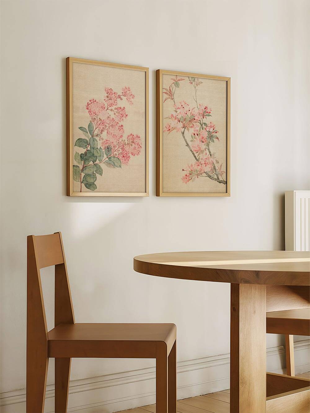 Zwei florale Kunstdrucke mit Kirschblüten hängen nebeneinander im Esszimmer. Die Illustrationen schaffen ein harmonisches Ambiente und unterstreichen den sanften Japandi-Stil.