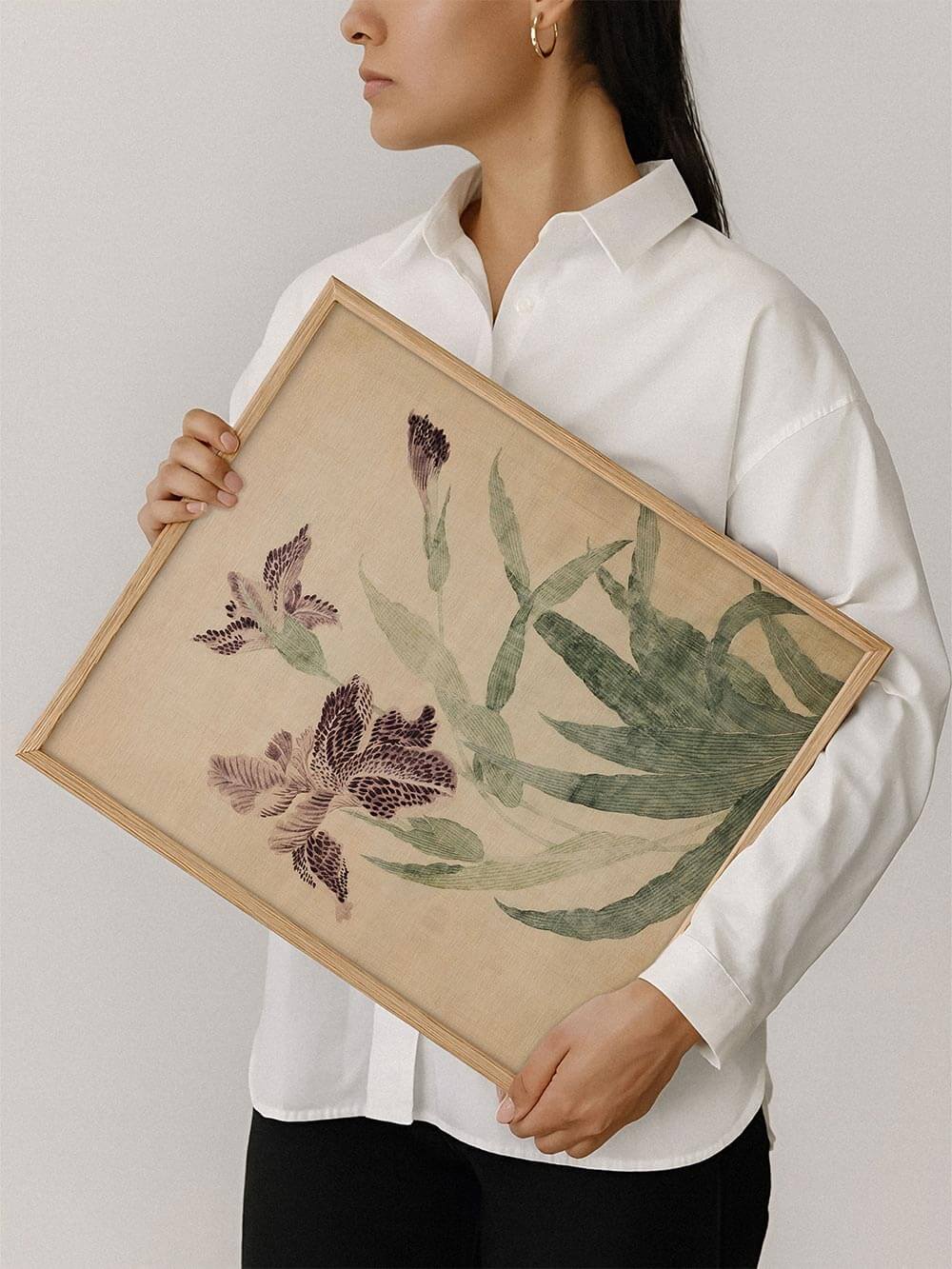 Kunstdruck mit botanischer Iris-Illustration wird von einer Person im hellen Holzrahmen gehalten. Die zarten Farben wirken beruhigend und zeitlos.