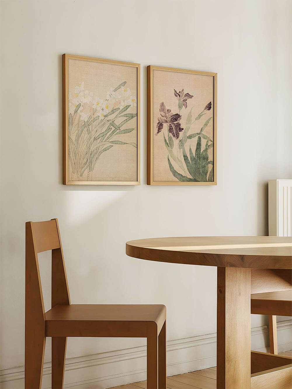 Zwei florale Kunstdrucke hängen nebeneinander an einer hellen Wand im Esszimmer. Die Illustrationen von Iris und Narzissen fügen sich harmonisch in das minimalistische Japandi-Design ein.