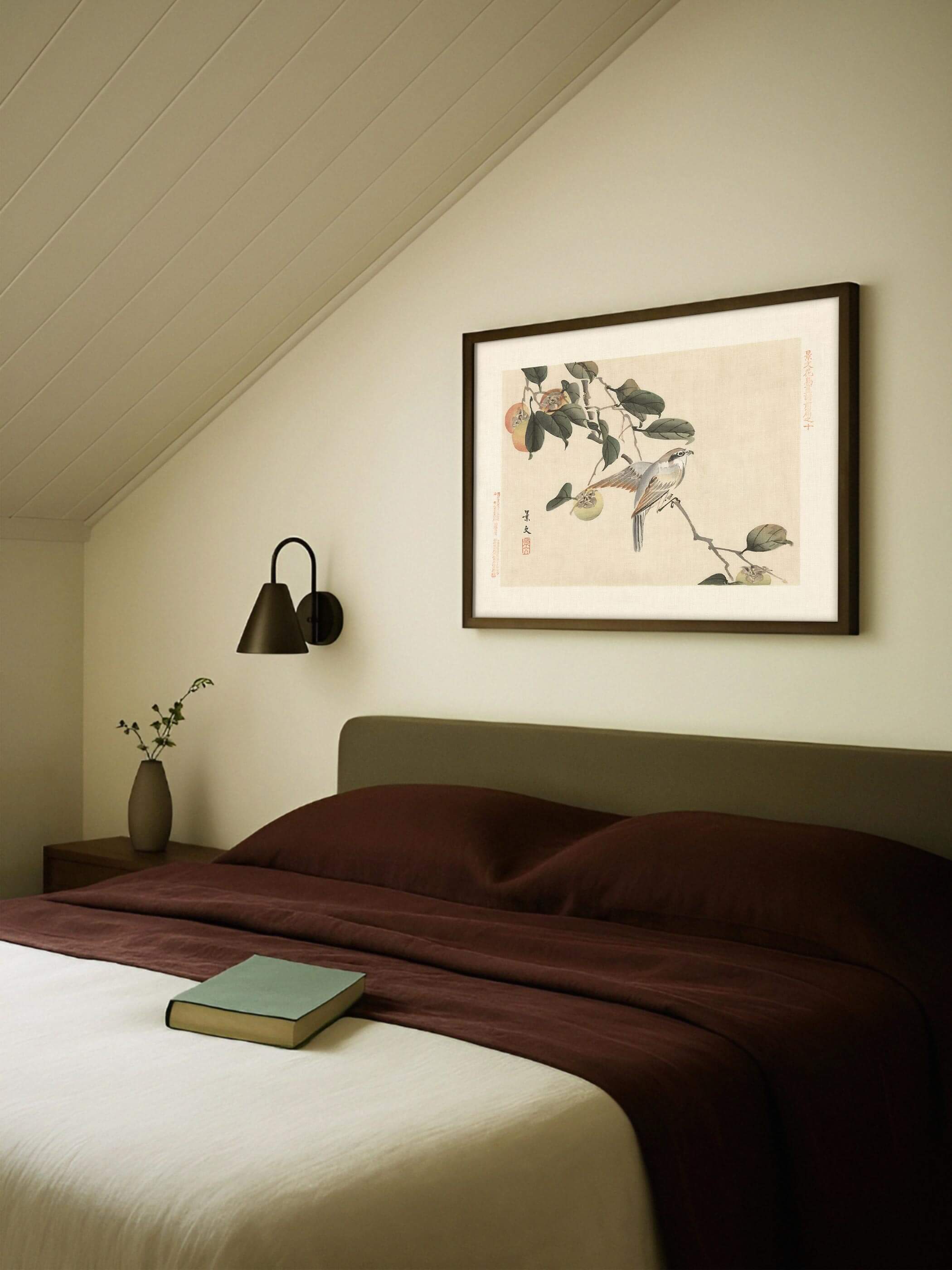 Chinoiserie Wandbild mit Vogel auf Kaki-Zweig hängt gerahmt über einem Bett mit dunkelroter Bettwäsche unter einer schrägen Dachschräge. Der warme Kunstdruck bringt eine ruhige, herbstliche Stimmung ins Schlafzimmer.