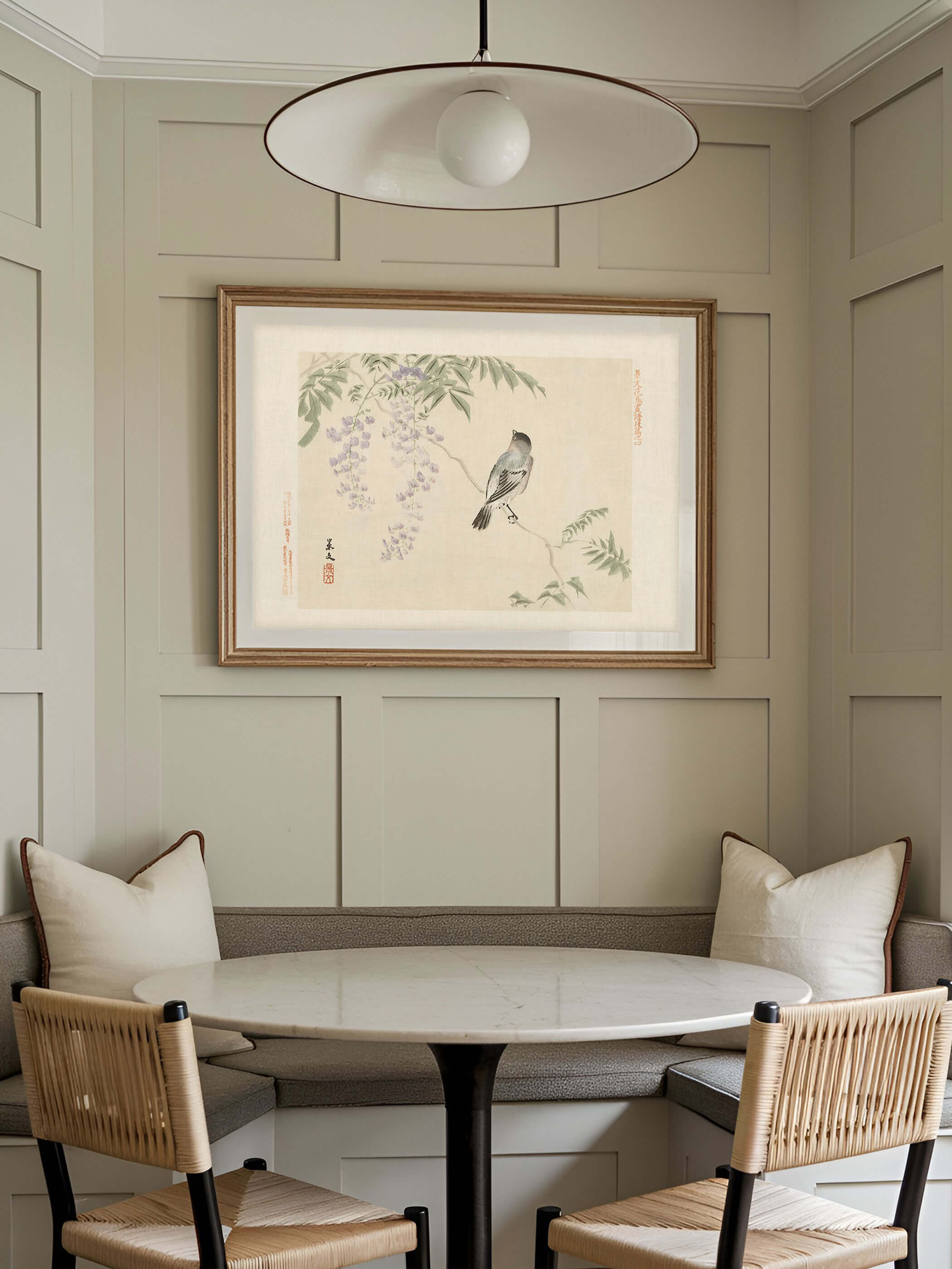 Chinoiserie Kunstdruck mit Vogel und Blauregen-Blüten hängt gerahmt über einer gepolsterten Sitzbank in einer getäfelten Essecke mit rundem Marmortisch. Das zarte Wandbild passt zu ruhigem, naturnahem Wohnstil.