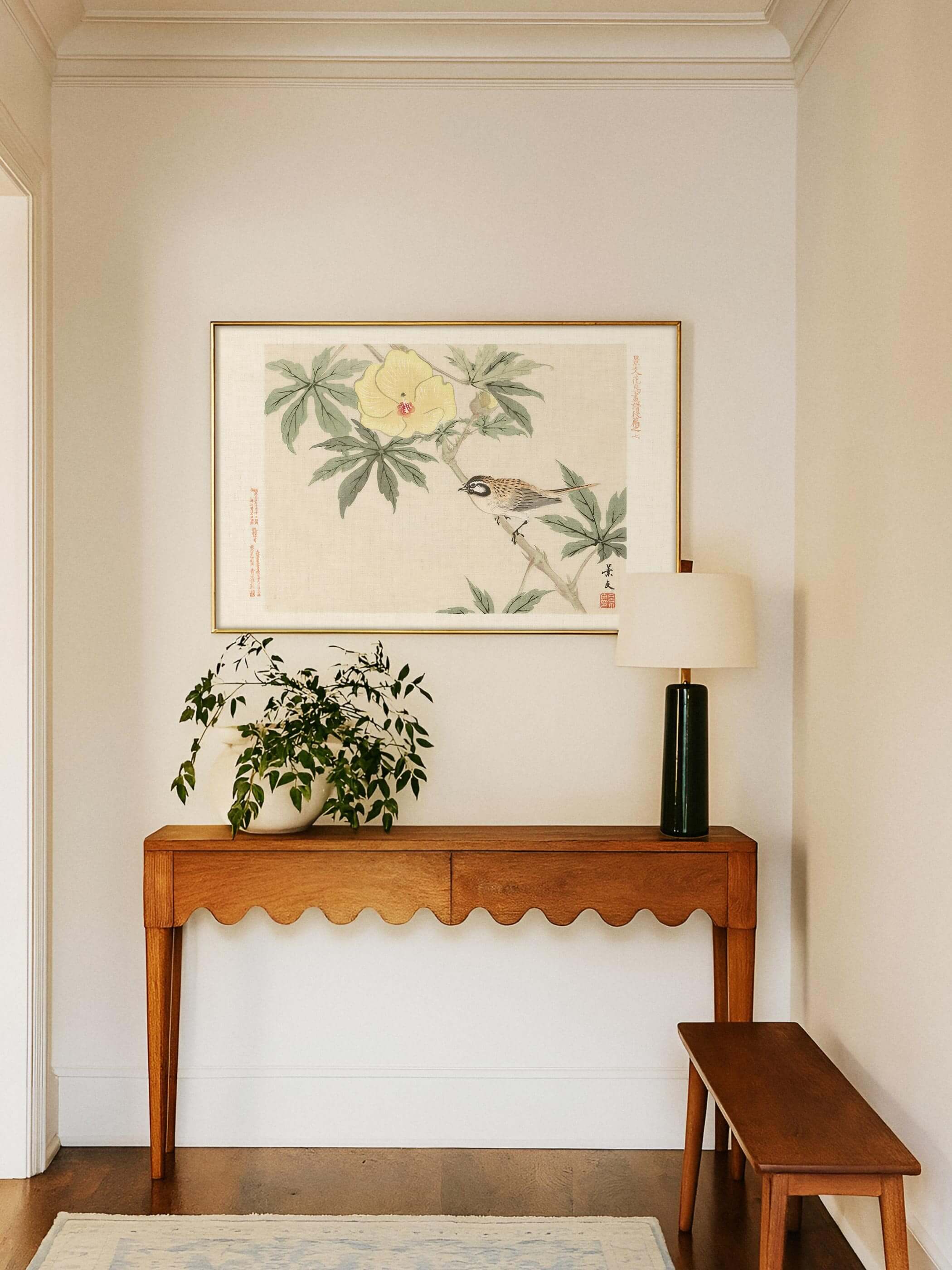 Chinoiserie Wandbild mit Vogel und Hibiskusblüte hängt gerahmt über einer Konsole mit Pflanze und Tischlampe im hellen Eingangsbereich. Der warme Kunstdruck verleiht dem Flur eine freundliche, natürliche Note.