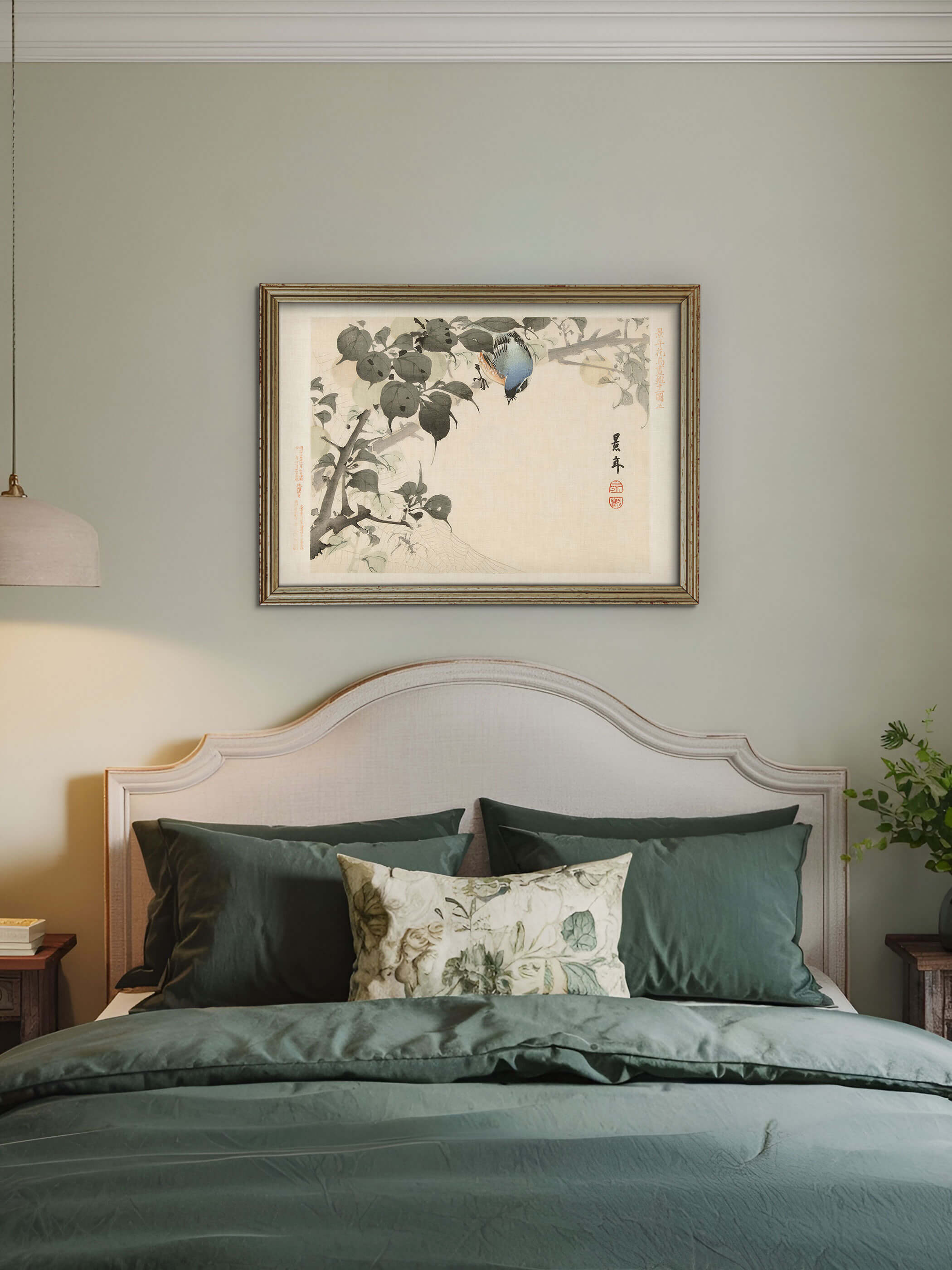 Gerahmter Chinoiserie Kunstdruck mit Vogel und Spinnennetz hängt über einem Bett mit dunkelgrüner Bettwäsche vor salbeigrüner Wand. Das ruhige Wandbild mit farbigem Akzent passt zu einem eleganten, gedämpften Schlafzimmer.