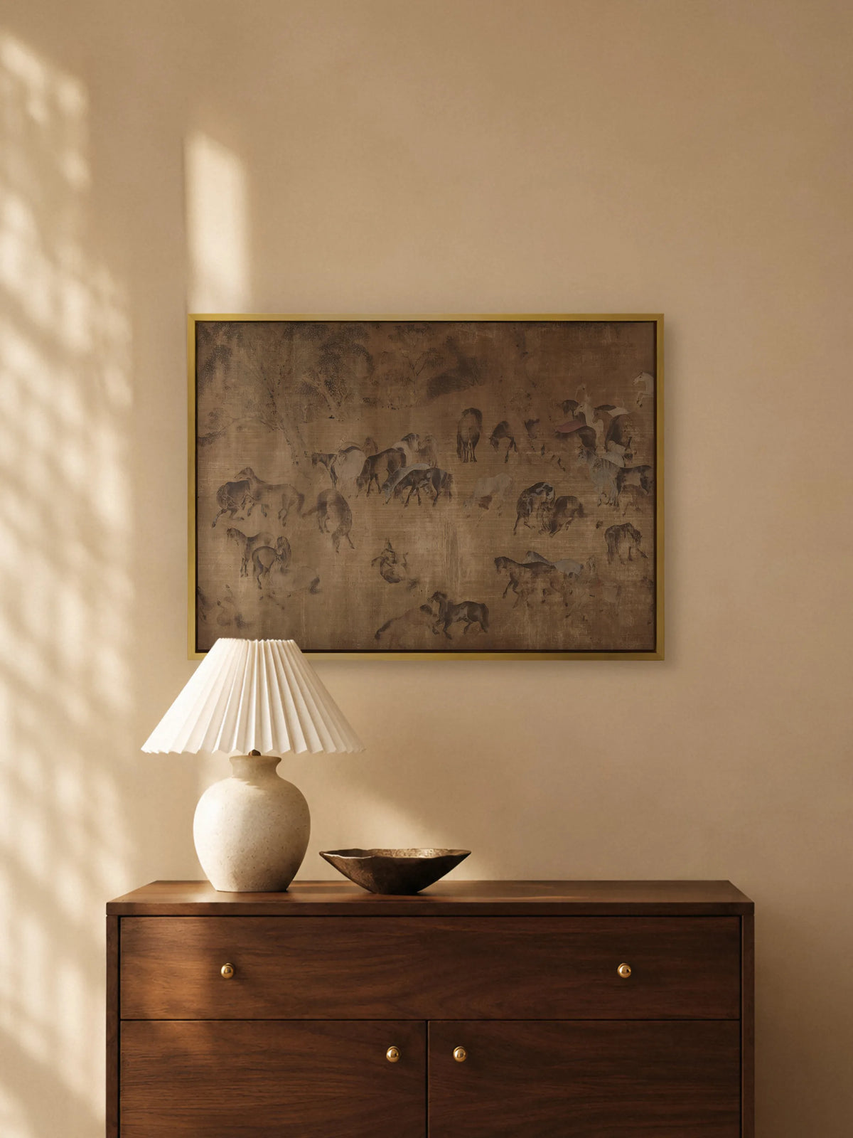 Leinwandbild mit chinesischer Pferdemalerei im goldenen Rahmen über einer dunklen Holzkommode mit Messingknöpfen. Auf der Kommode stehen eine Keramiklampe mit weißem Plisseeschirm und eine flache Bronzeschale.