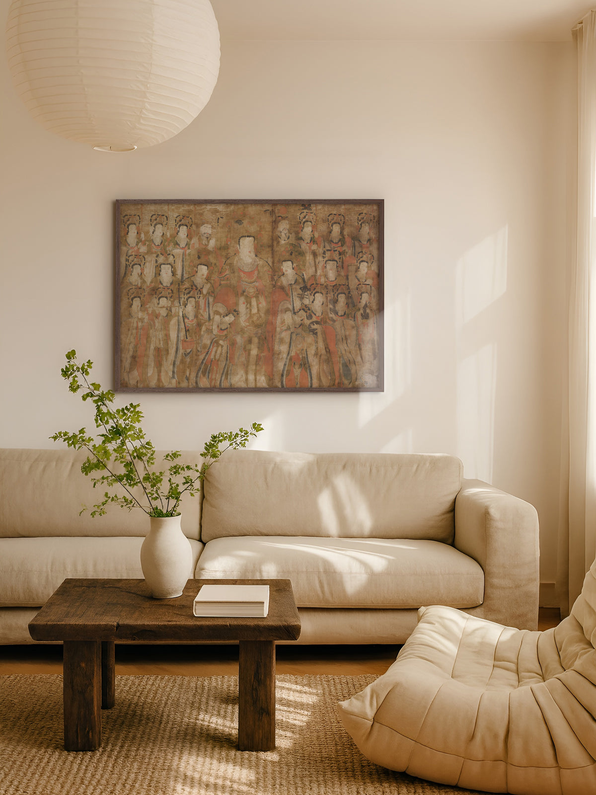 Asiatisches Wandbild im dunklen Holzrahmen über einem beigen Sofa im hellen Wohnzimmer, davor ein rustikaler Couchtisch mit weißer Vase und Zweigen unter einer Papierlampe. Die erdigen Töne des Kunstdrucks passen zu einem warmen Japandi Wohnstil.