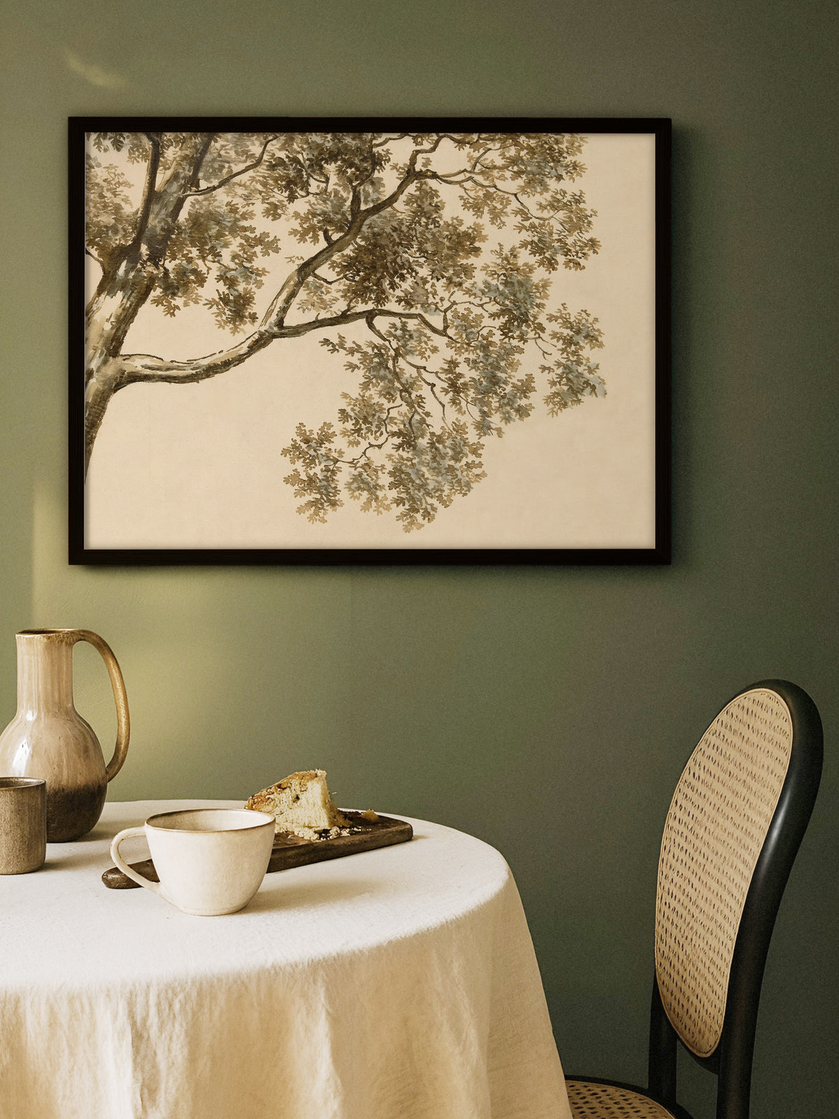 Baum Zeichnung als Poster im schwarzen Rahmen an einer dunkelgrünen Wand über einem runden Tisch mit Leinentischdecke, Keramikkrug und Tasse, daneben ein Stuhl mit Wiener Geflecht. Vor dem Grün wirken die Sepiatöne warm und moody.