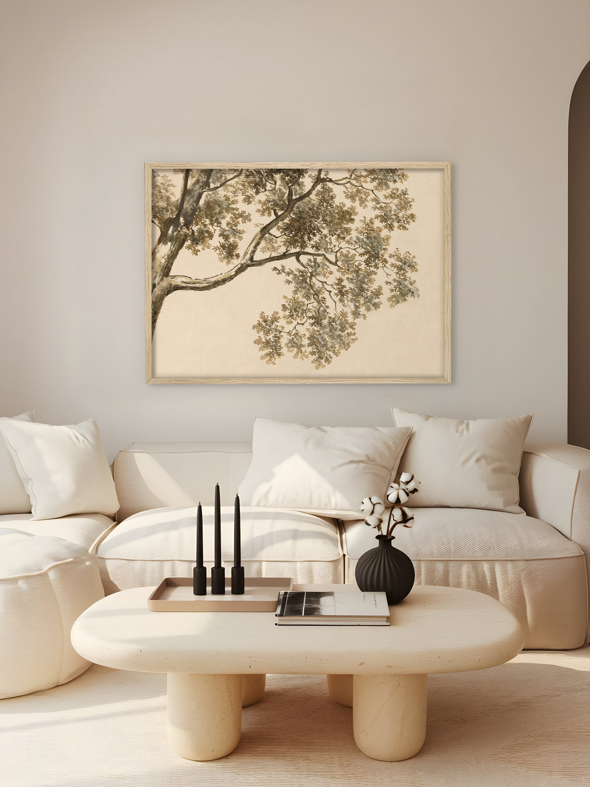 Kunstdruck mit Baumkrone im Rahmen aus hellem Holz über einem cremeweißen Sofa, davor ein runder Steintisch mit schwarzen Kerzen und einer Vase mit Baumwollzweigen. Das Querformat fügt sich in das helle Wabi Sabi Wohnzimmer ein.