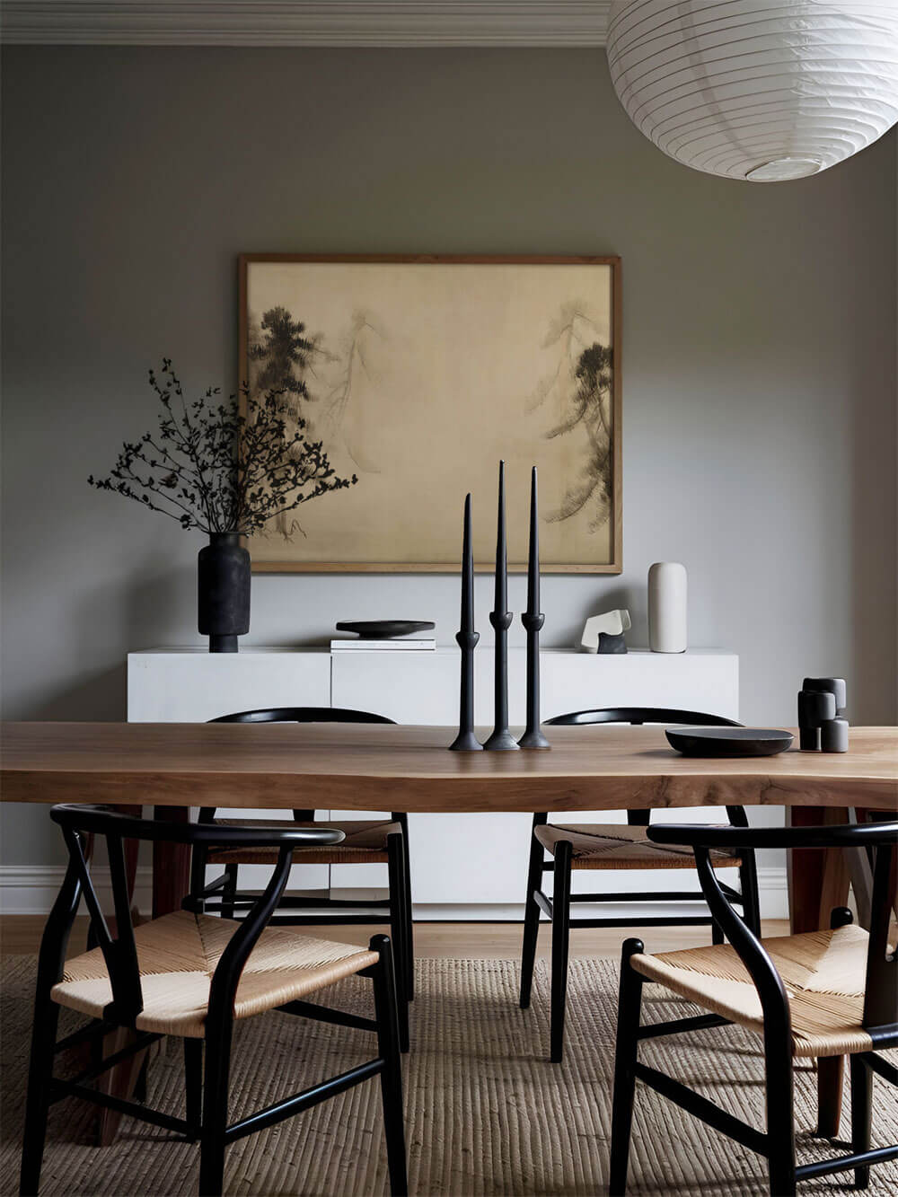 Esszimmer mit Wabi-Sabi Kiefernskizze als Wandbild, eingerahmt über einem Holz-Esszimmertisch mit schwarzen Kerzenständern und minimalistischer Dekoration.
