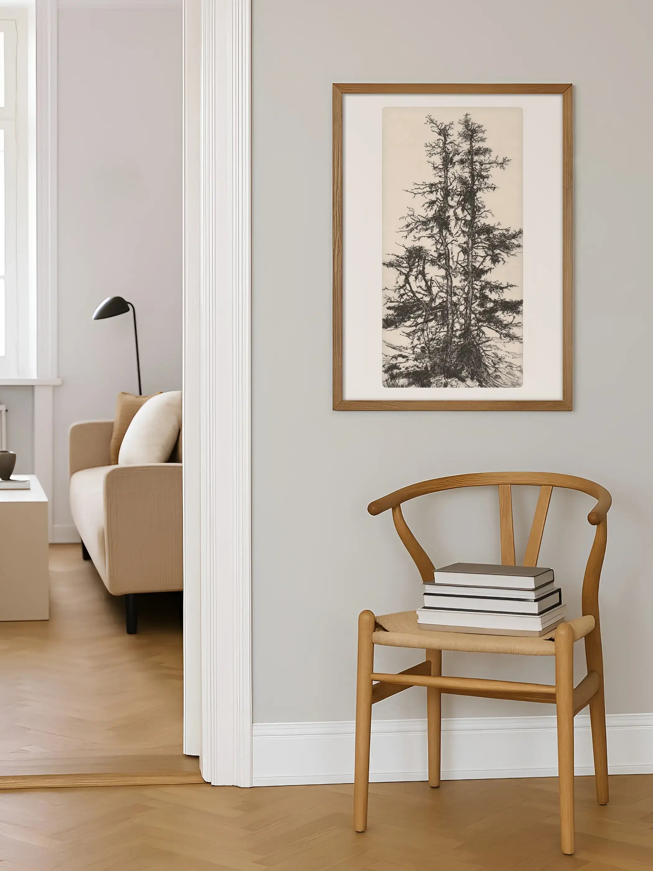 Die filigrane Schwarzweißzeichnung eines schlanken Baumes hängt über einem Holzstuhl in einem hellen Wohnraum. Der botanische Kunstdruck ergänzt skandinavische, Japandi und minimalistische Einrichtungen mit natürlicher Ruhe.